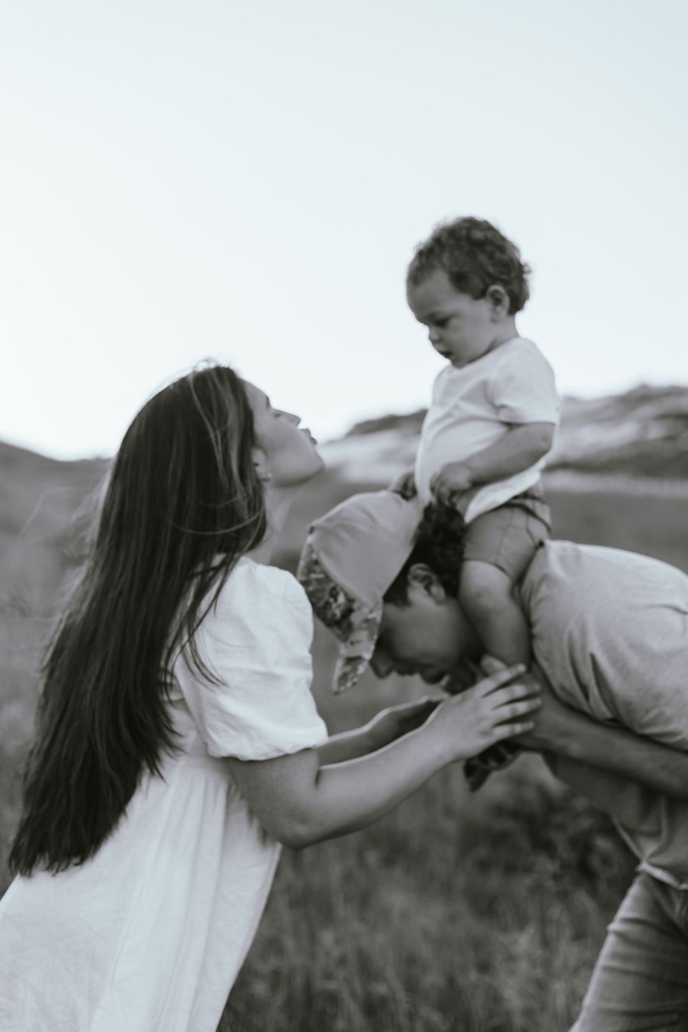 A tender family moment captured in black and white as they play together outdoors in a grassy field.