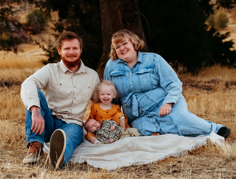 A family wearing casual clothing sits together on a blanket in a golden autumn field during sunset.