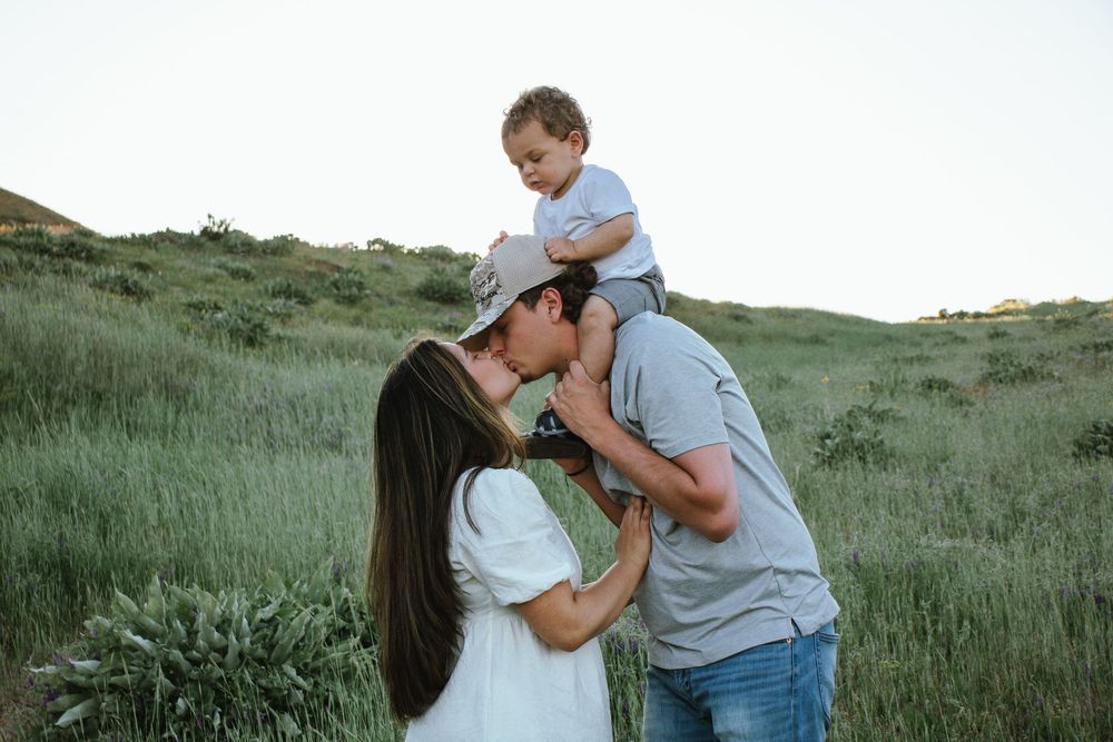 A family of three sharing an intimate moment together on a grassy hillside during golden hour.