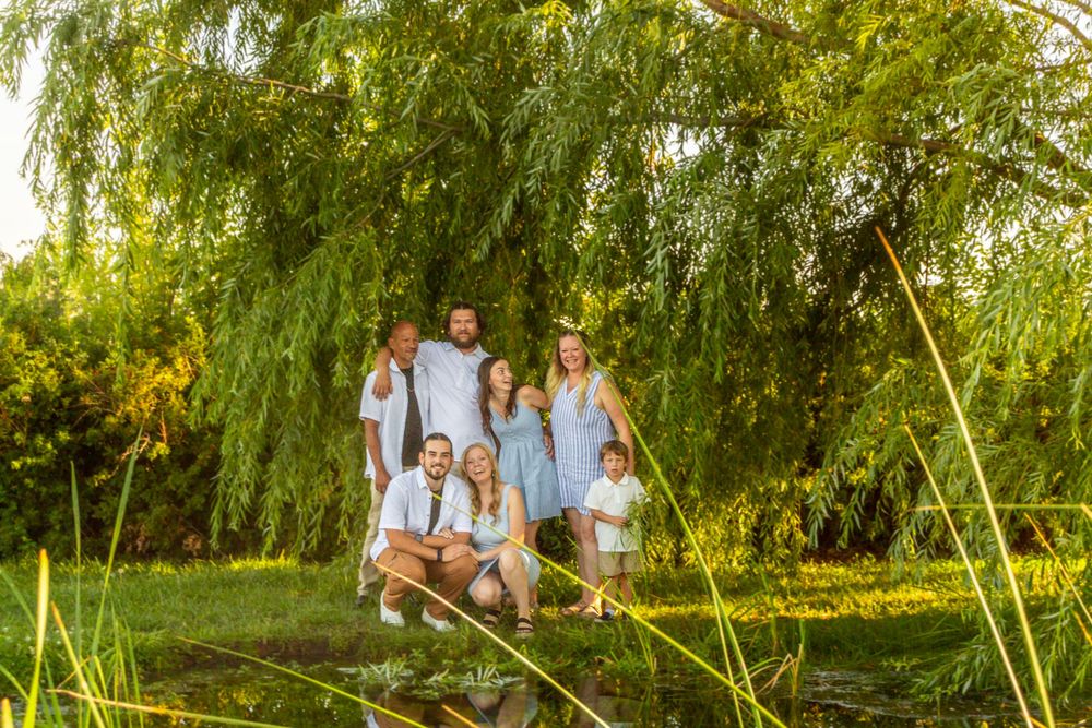 A group poses together under a large weeping willow tree at sunset in a park setting.