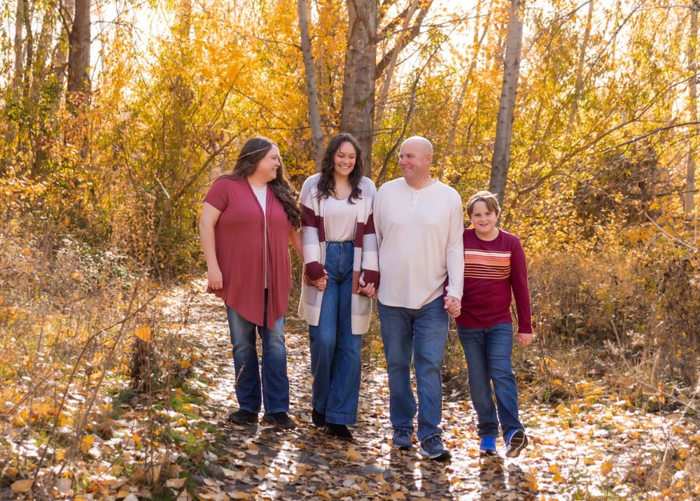A group in coordinating fall outfits walks together on a path surrounded by golden autumn trees and fallen leaves.