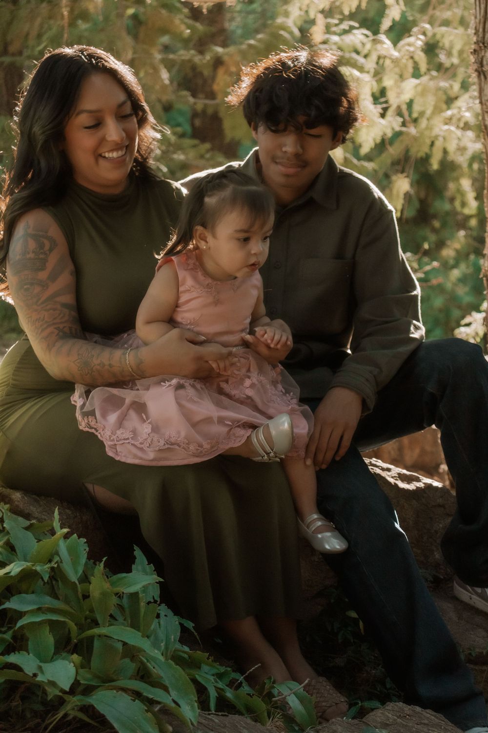 Family sharing a tender moment together outdoors with baby in pink dress while sitting in natural garden setting.