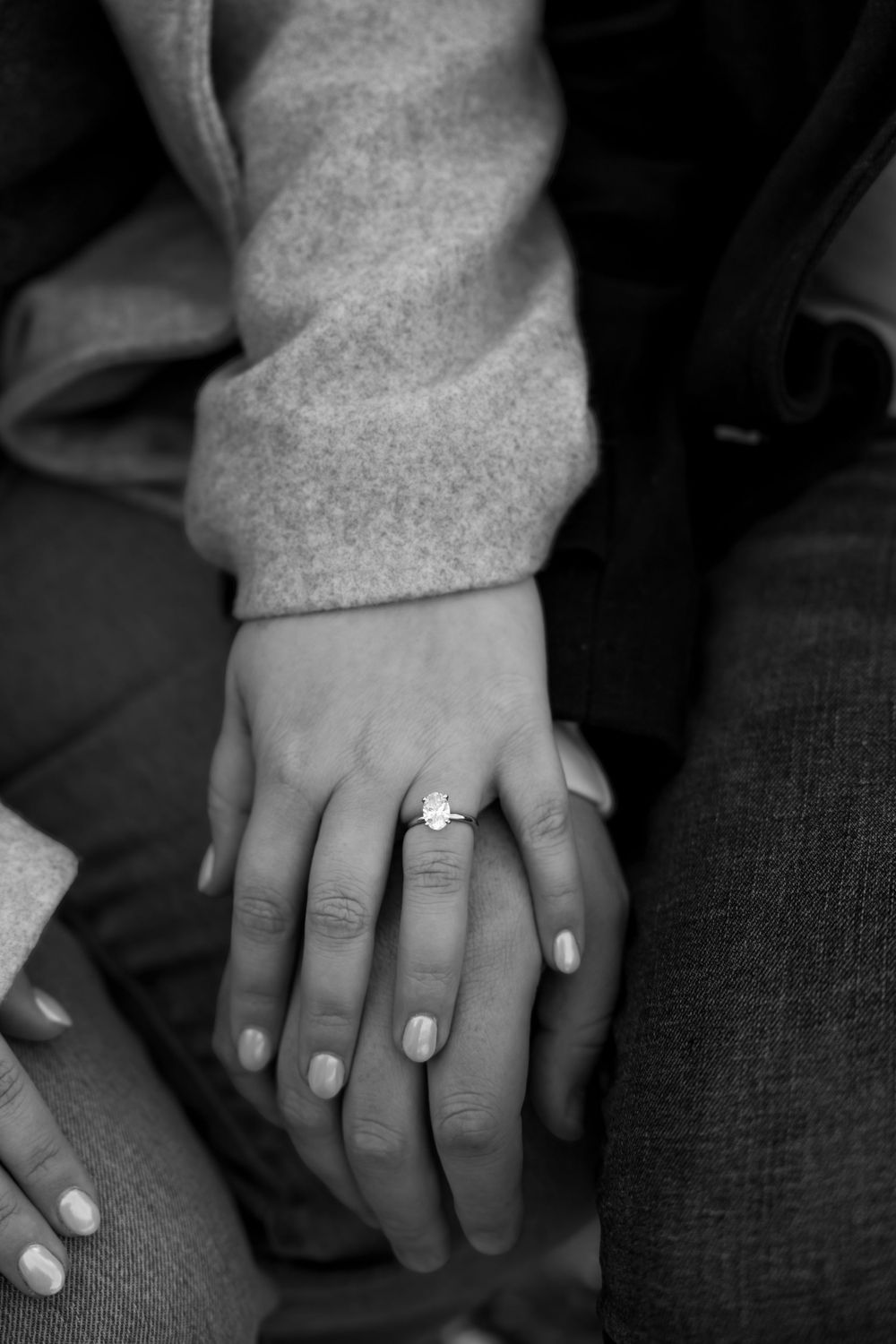 Black and white photo of two hands gently clasped together, with one hand wearing an engagement ring.