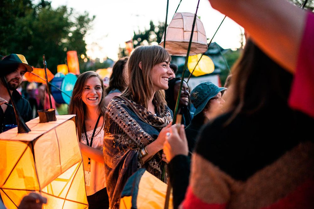 Festival attendees holding colorful paper lanterns at dusk during an outdoor celebration event.