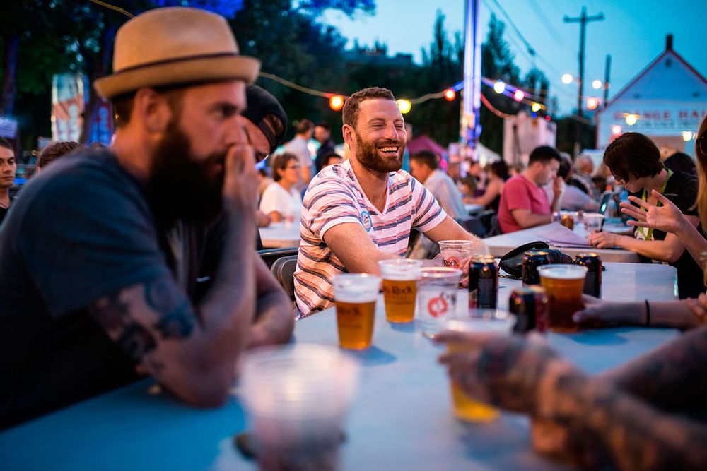 Friends sharing drinks and conversation at an outdoor beer garden during sunset.