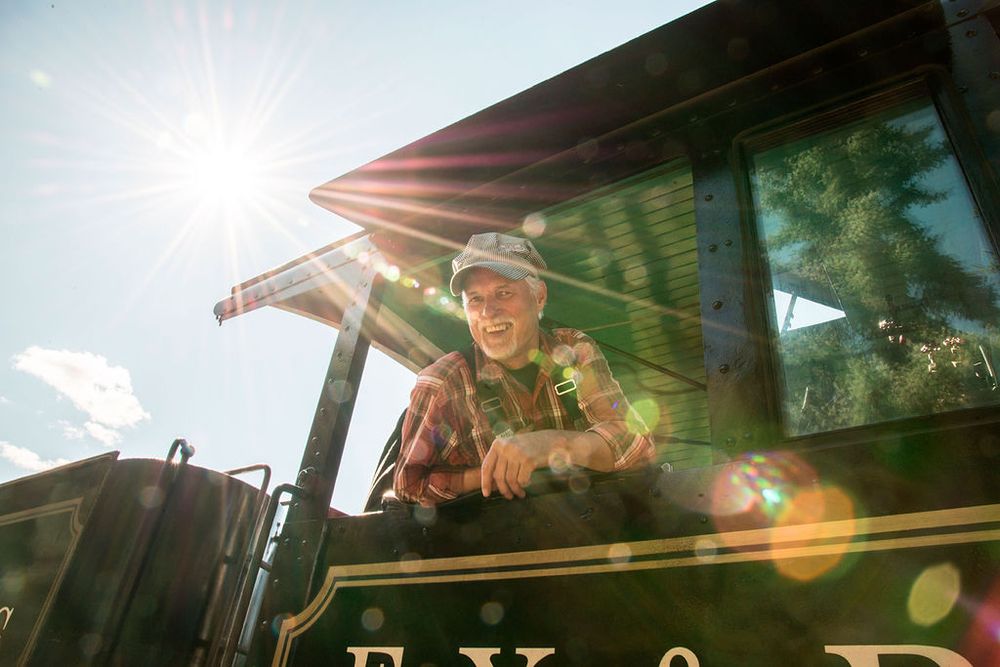 Railroad conductor looking out the window of a train engine on a sunny day.