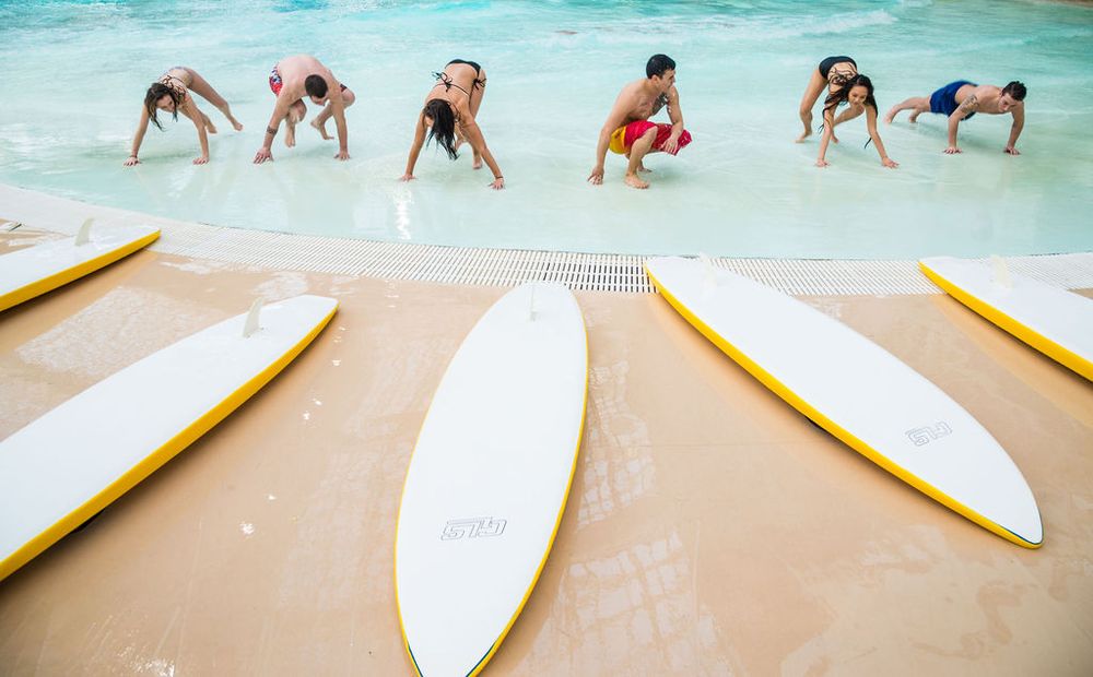 Group stretching on beach beside surfboards during morning surf lesson.