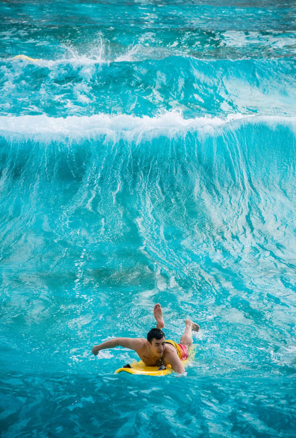 Surfer riding a bright turquoise wave on a yellow surfboard.