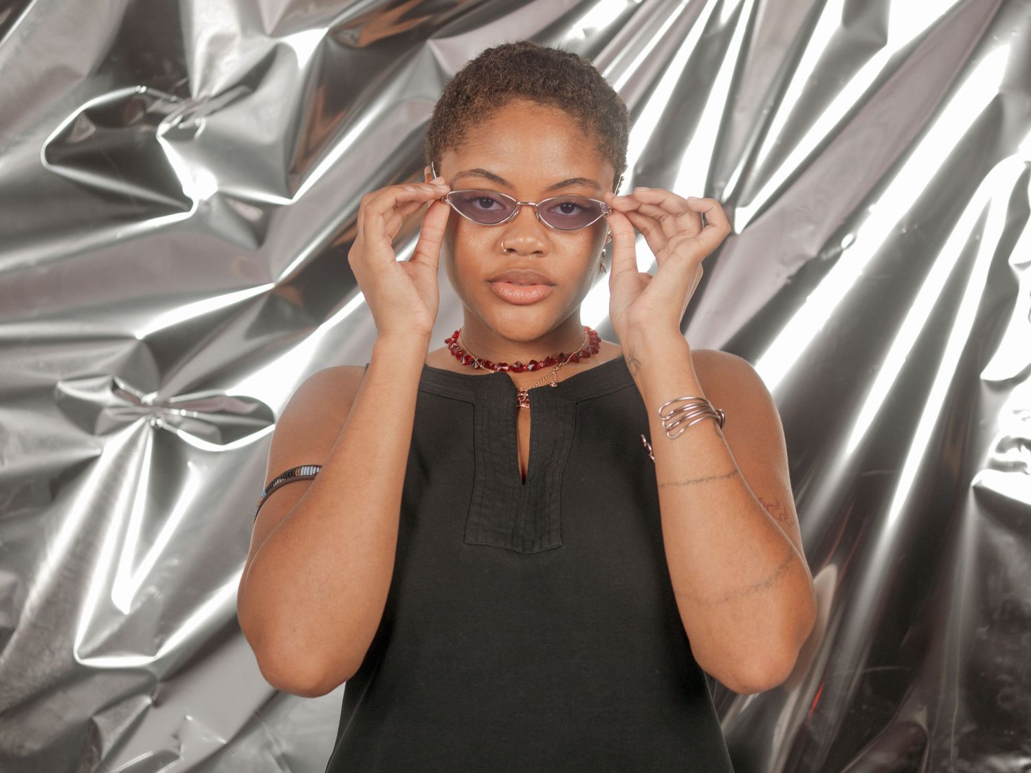 Someone adjusting trendy glasses against a metallic silver backdrop in a studio setting.