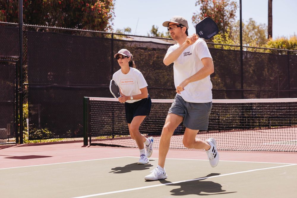 Two players engaged in a tennis match on an outdoor court during a sunny autumn day.