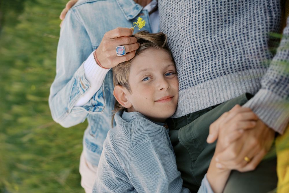 Child holding onto adult wearing a grey sweater while laughing outdoors in a playful moment.