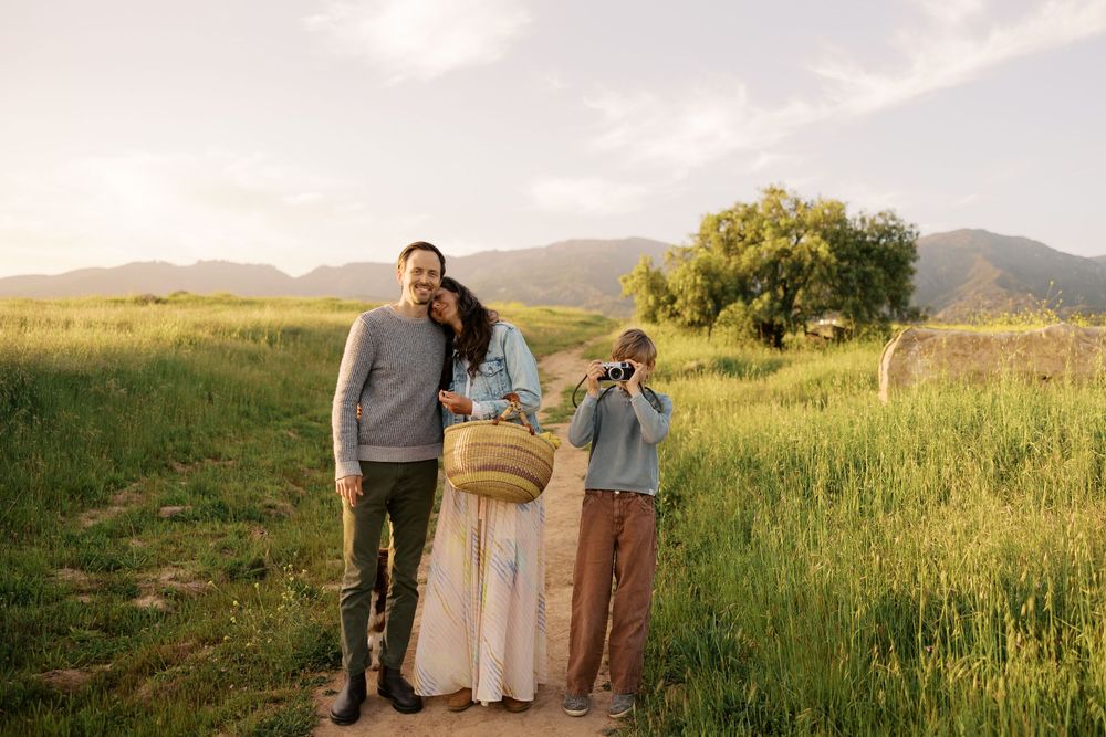 Couples stand together in a golden grassy field with mountains in the distance during sunset.