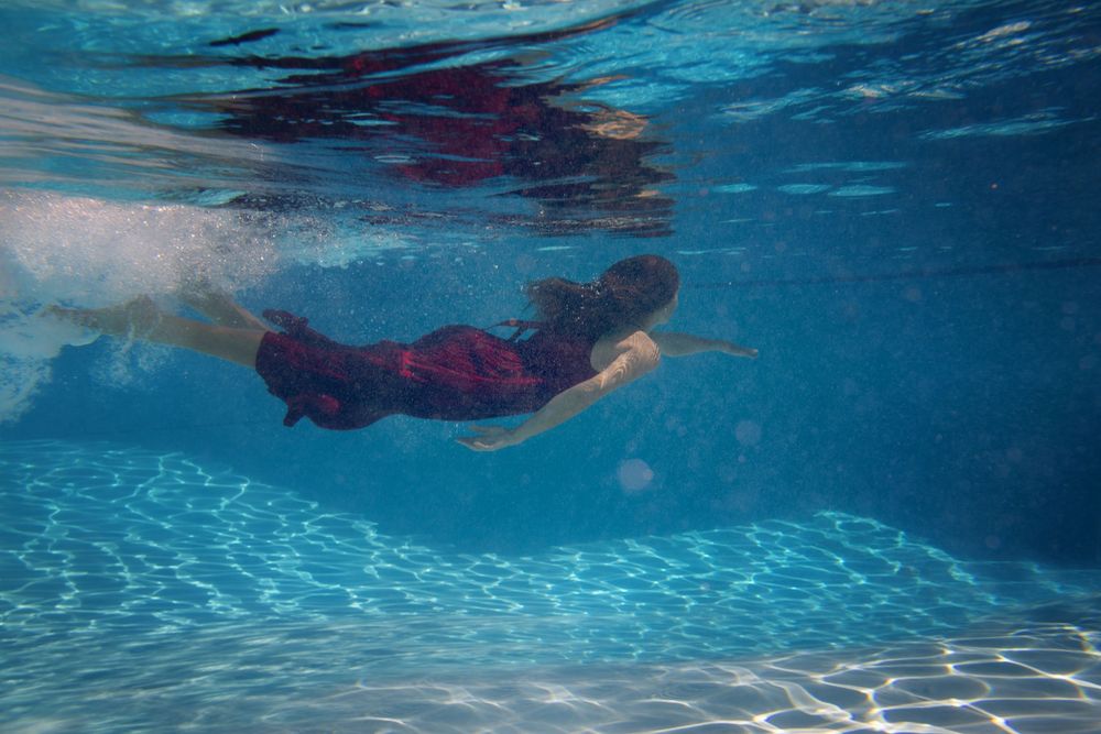 Multiple underwater shots showing swimmers moving gracefully beneath the surface of a blue pool.