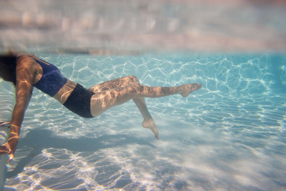 Underwater view of swimmers gliding through a pool's crystal clear blue water.