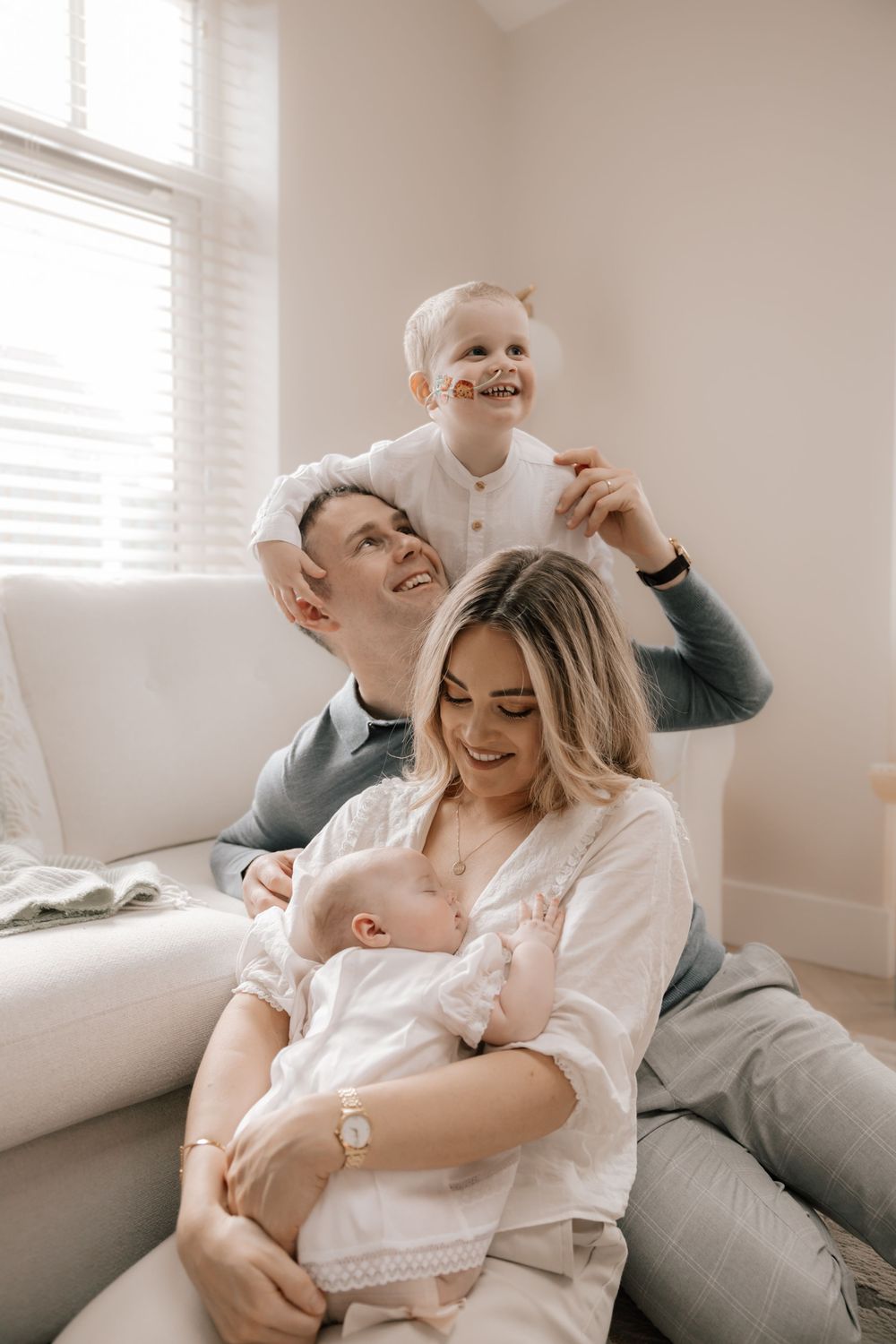 A joyful family moment captured in soft neutral tones as they relax together on a white couch near a window.