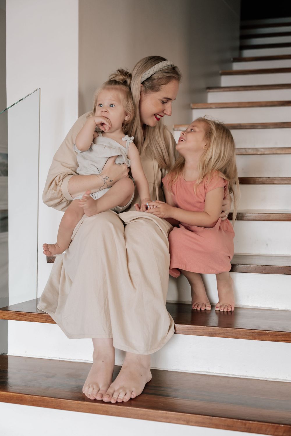 Three people share an intimate moment together while sitting on wooden stairs in a modern home interior.