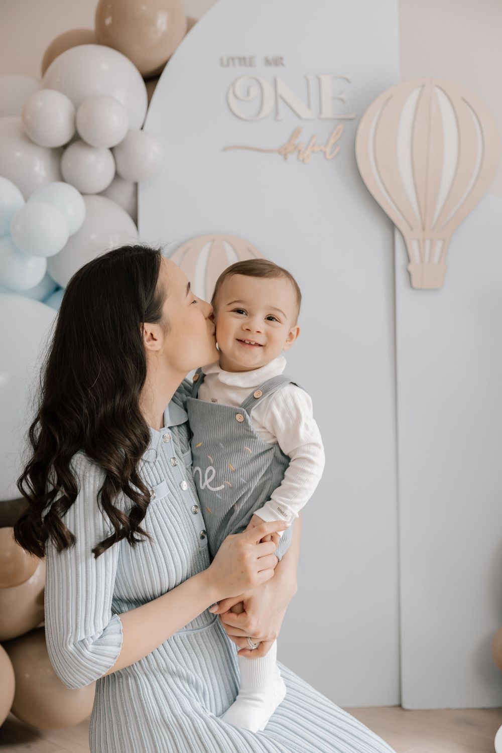 Family portrait with balloons and hot air balloon decor showing tender moment against pastel backdrop.