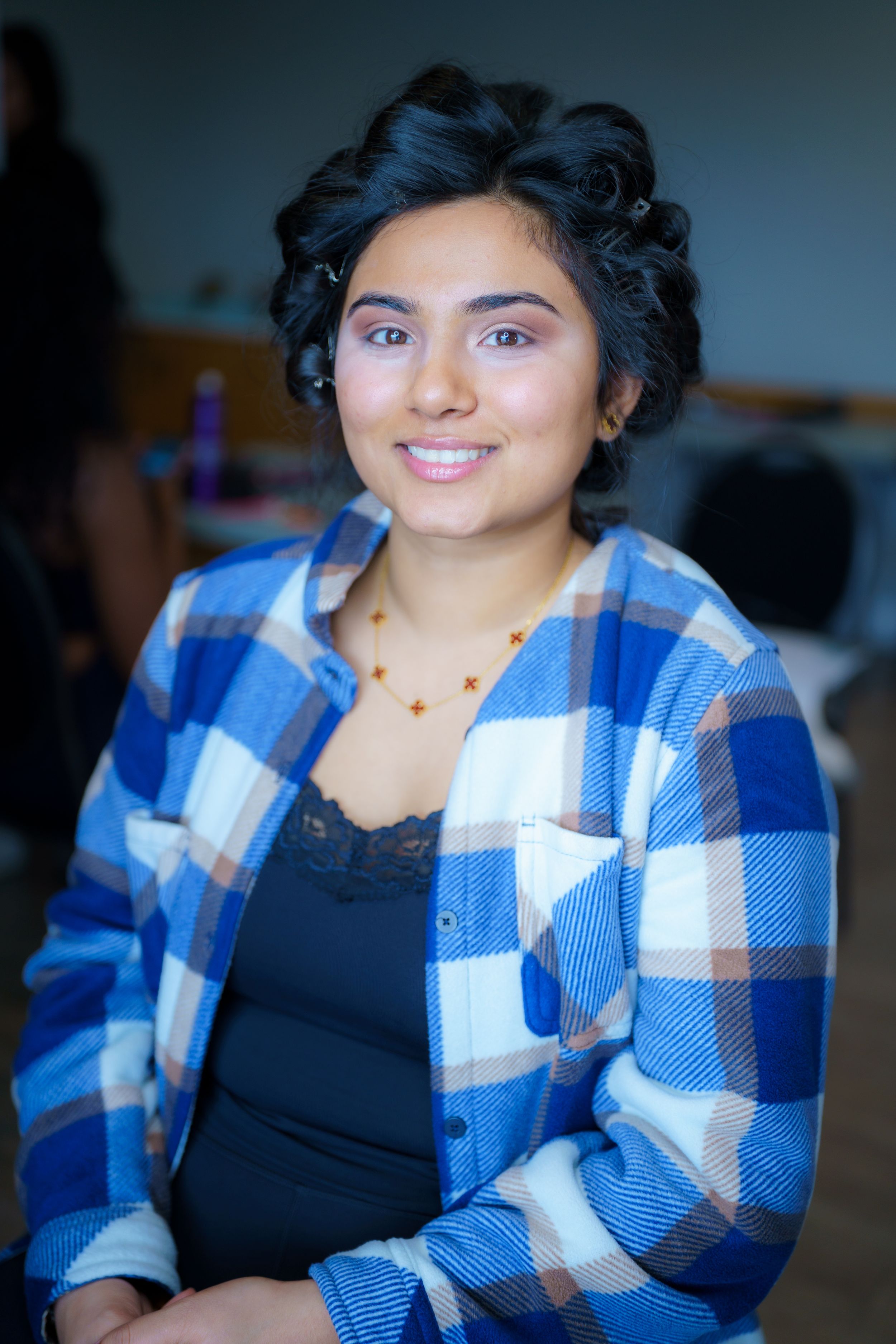 Woman wearing blue and white plaid flannel shirt over black top with beaded necklace smiles at camera.