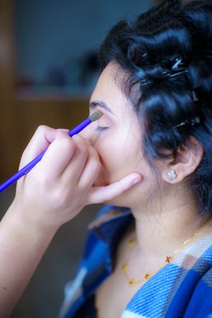 A hand applies eye makeup with a blue makeup brush in a side profile view during a beauty session.