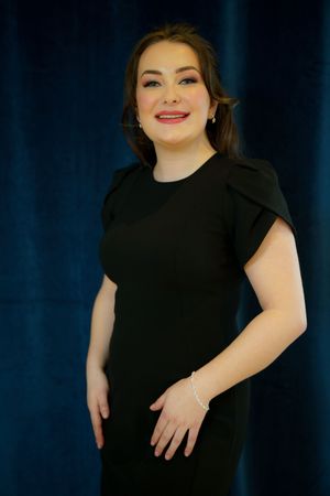 A person in a black dress poses against a dark blue backdrop for a professional portrait.