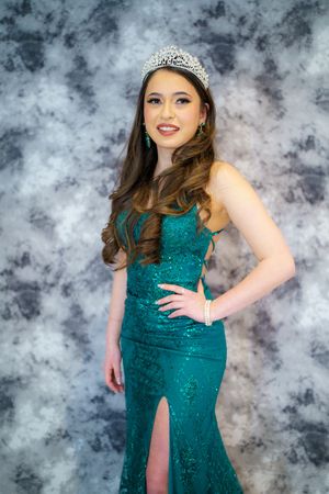 Sparkling teal evening gown with slit and tiara against misty gray background.