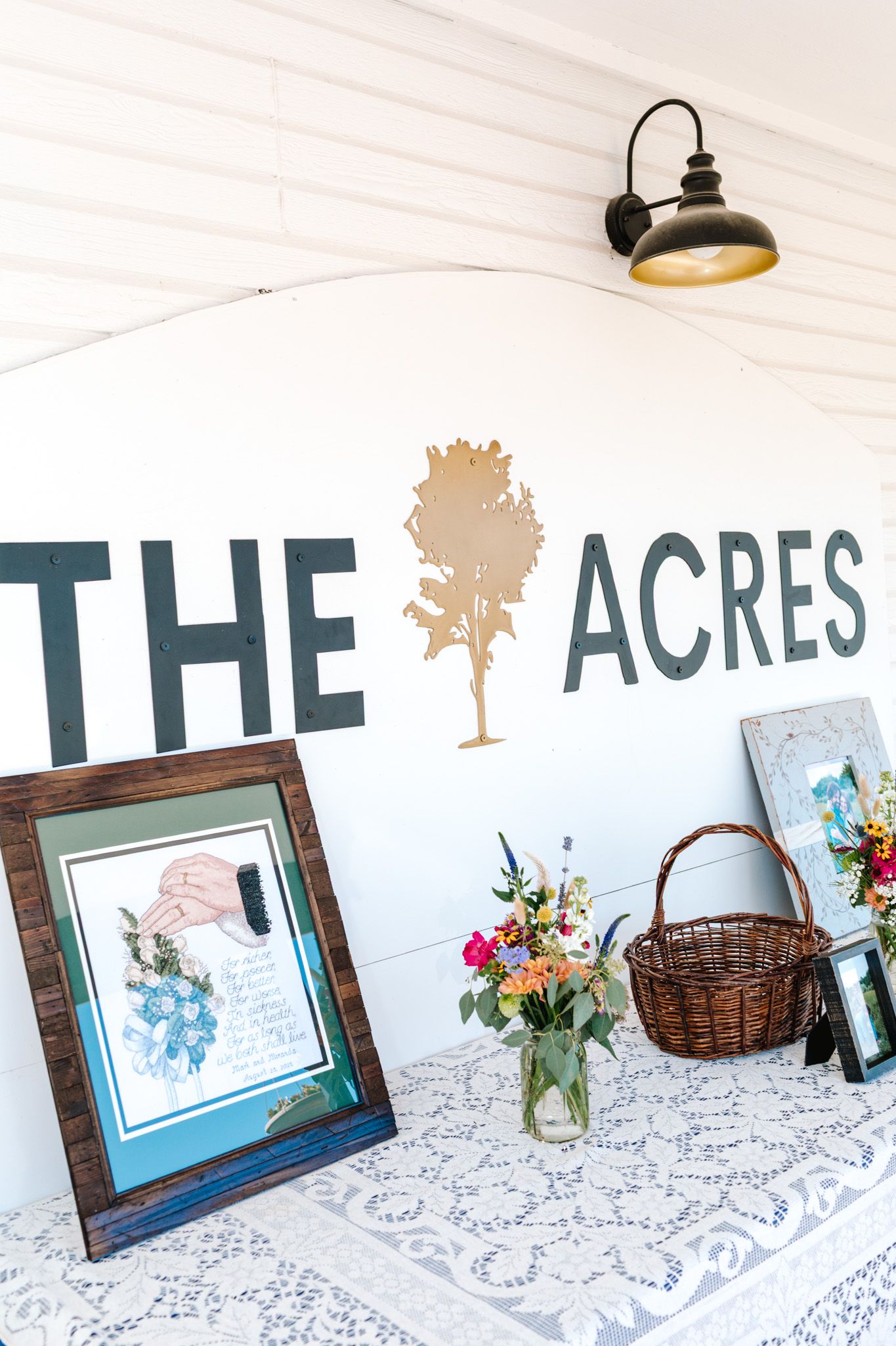 Rustic wedding venue sign reading The Acres with floral arrangements and lace tablecloth decor.