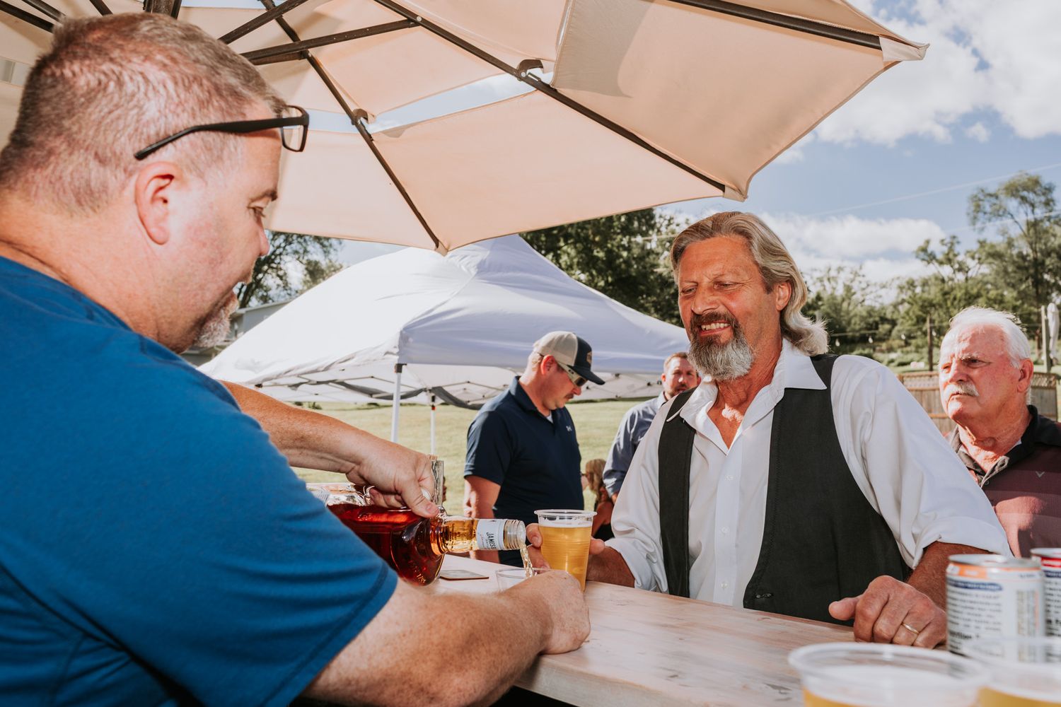 Men socializing at an outdoor bar under a white umbrella on a sunny day.