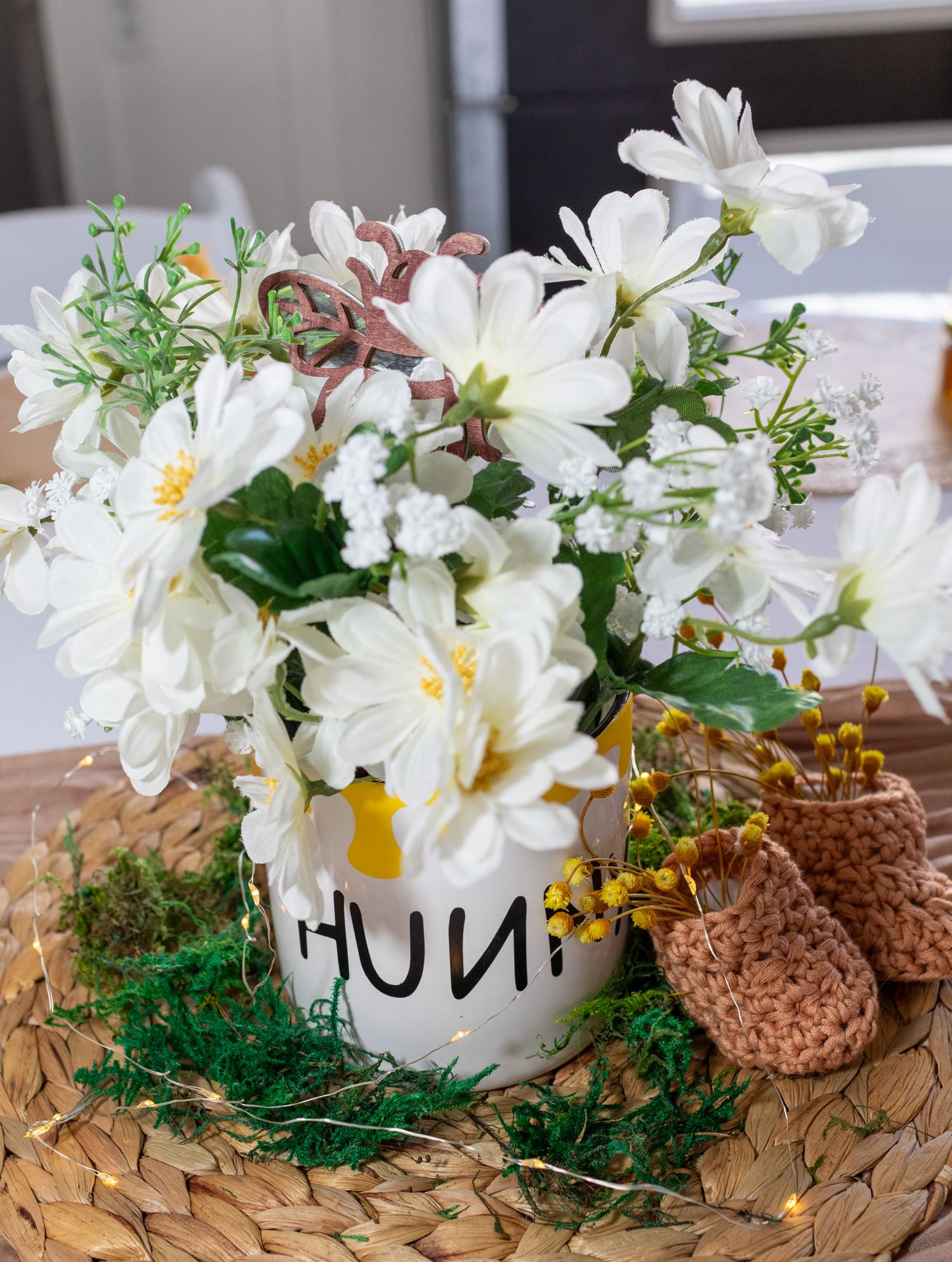 White daisy arrangement in a Winnie the Pooh honey pot with tiny crocheted baby shoes.
