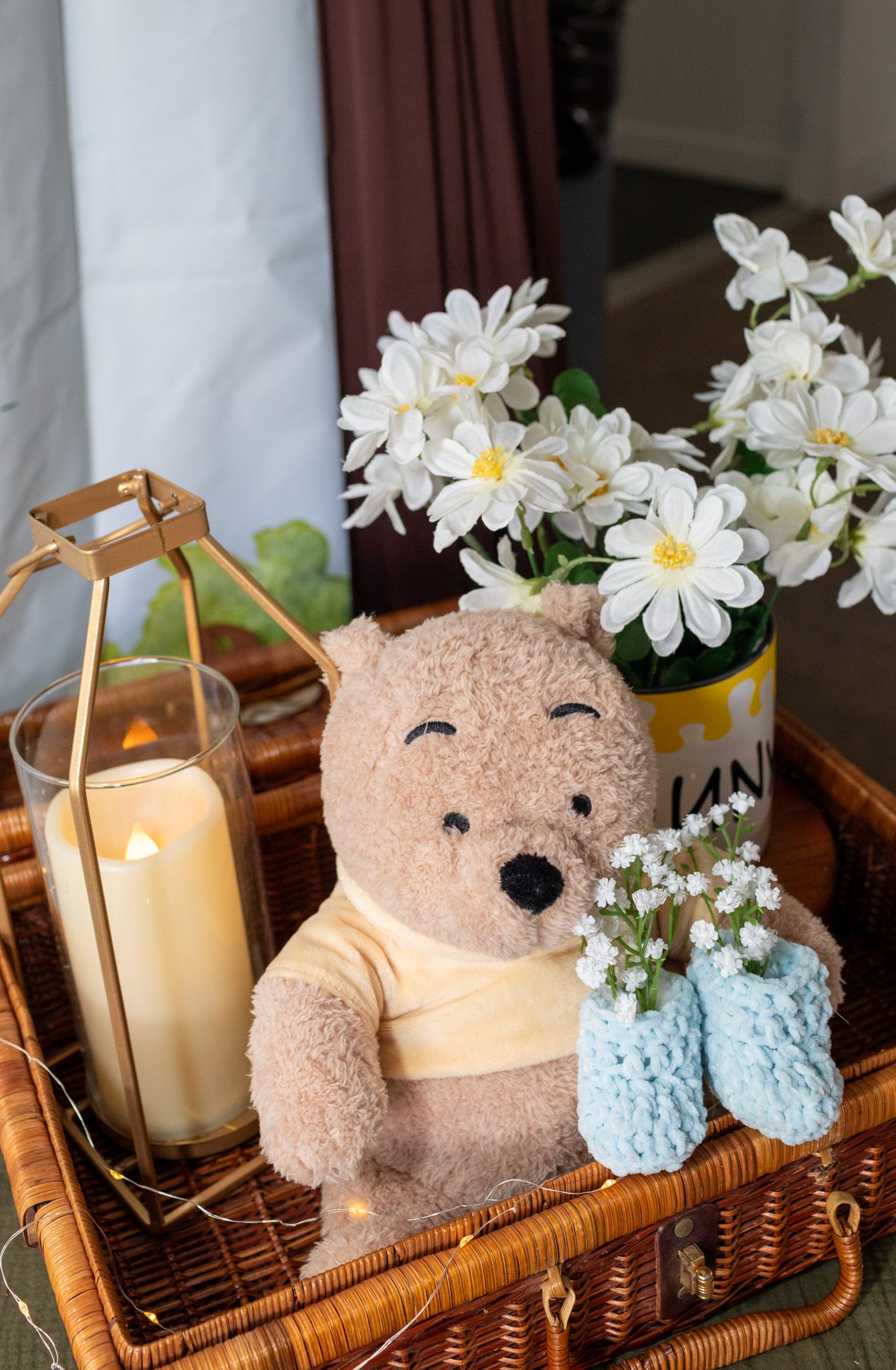 Winnie the Pooh stuffed bear in a wicker basket with white flowers and a candle.
