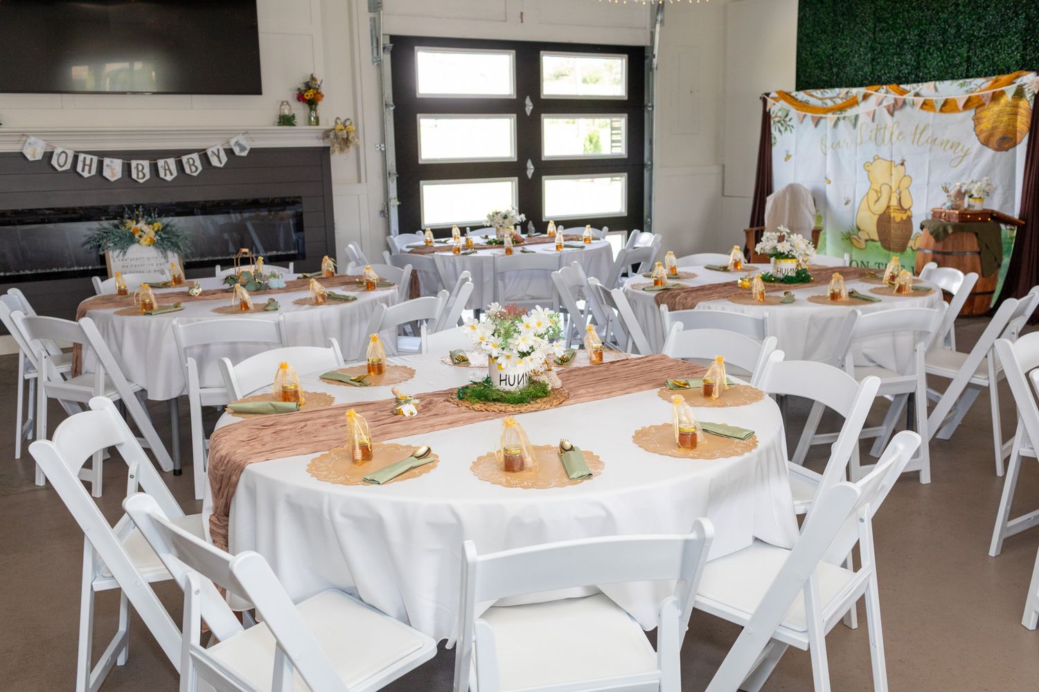 Elegant baby shower venue with round tables, white linens, gold accents, and floral centerpieces.