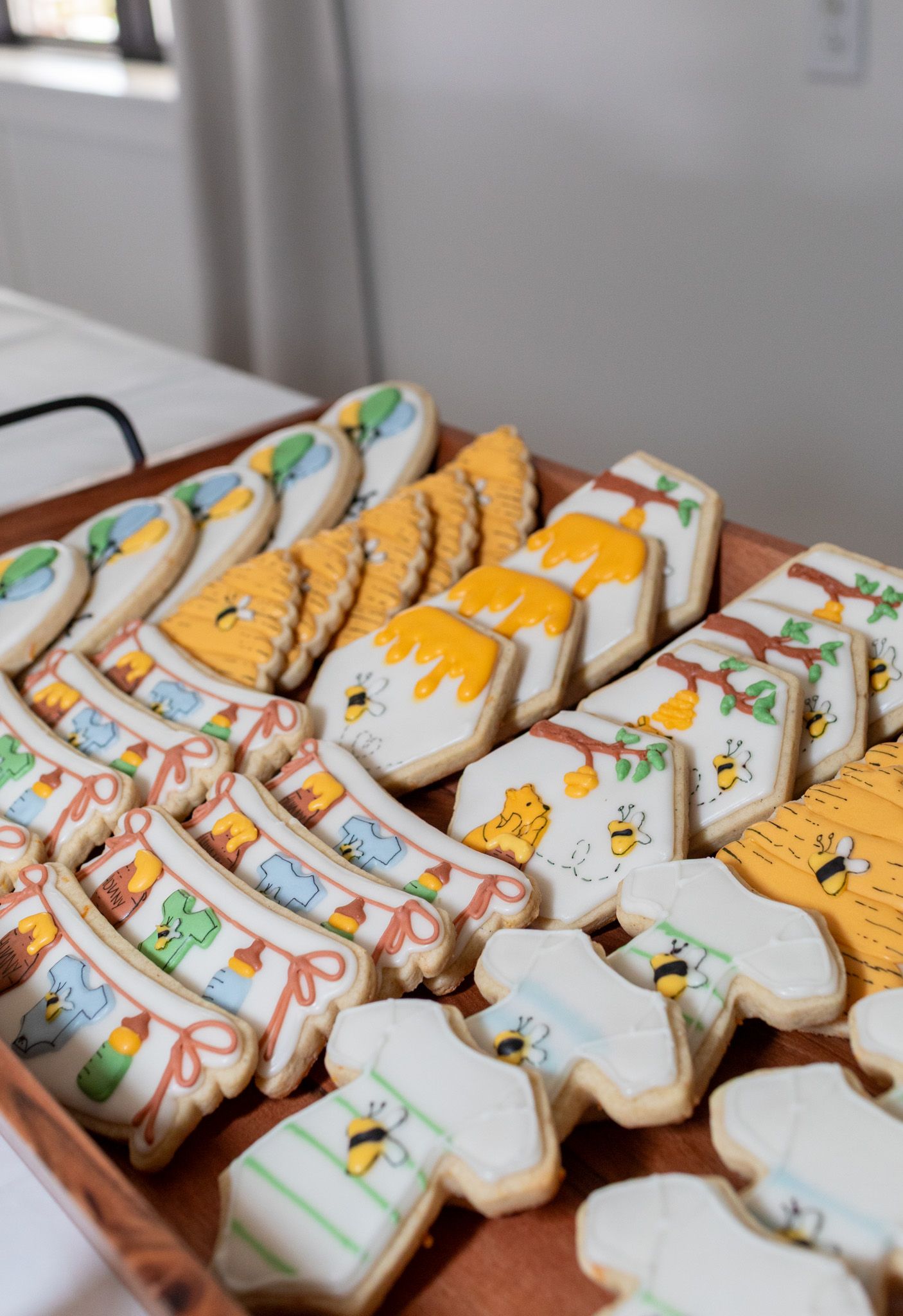 Decorated sugar cookies with Winnie the Pooh and honey bee designs arranged on a wooden tray.