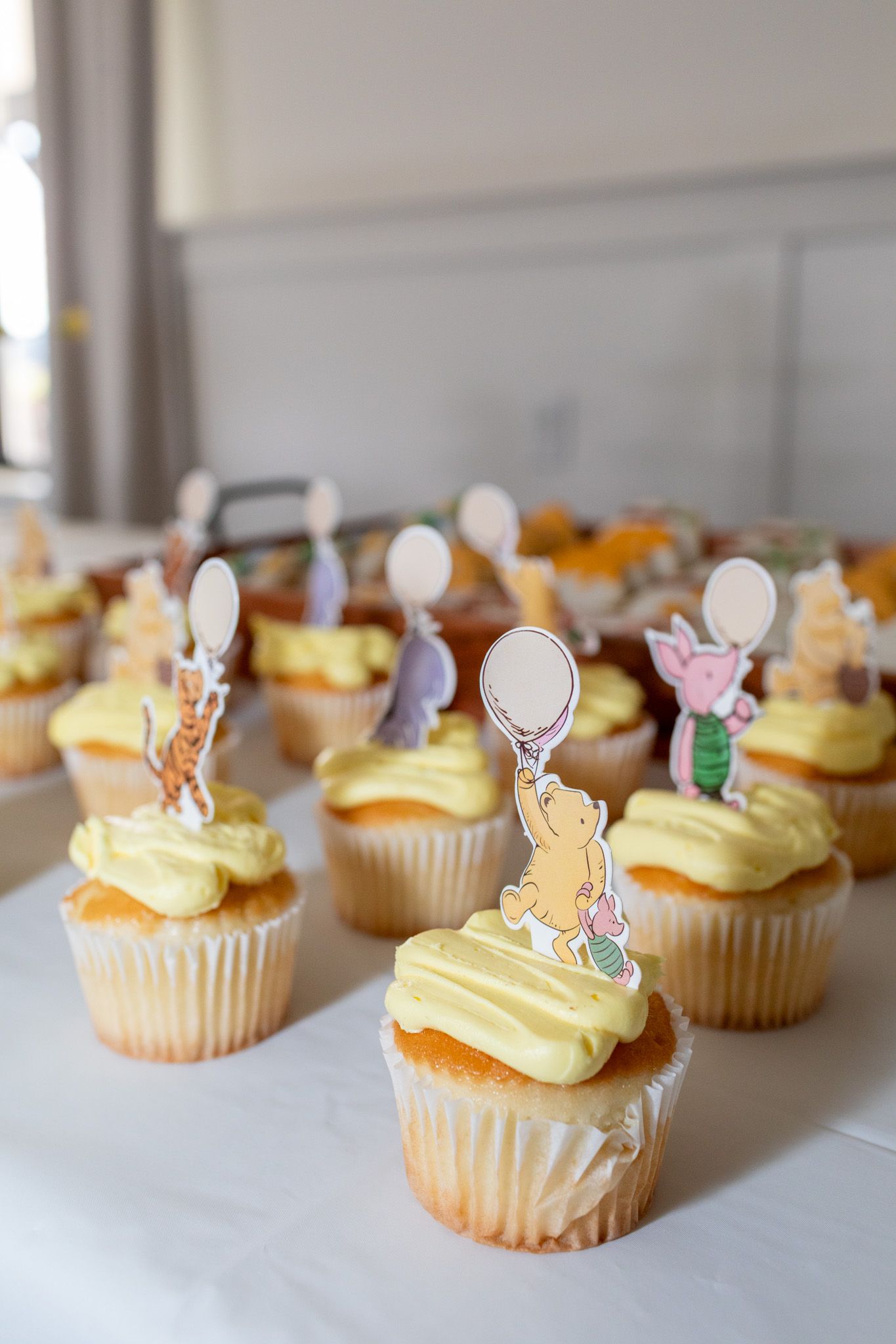 Close-up of vanilla cupcakes with yellow frosting topped with classic Winnie the Pooh character picks.