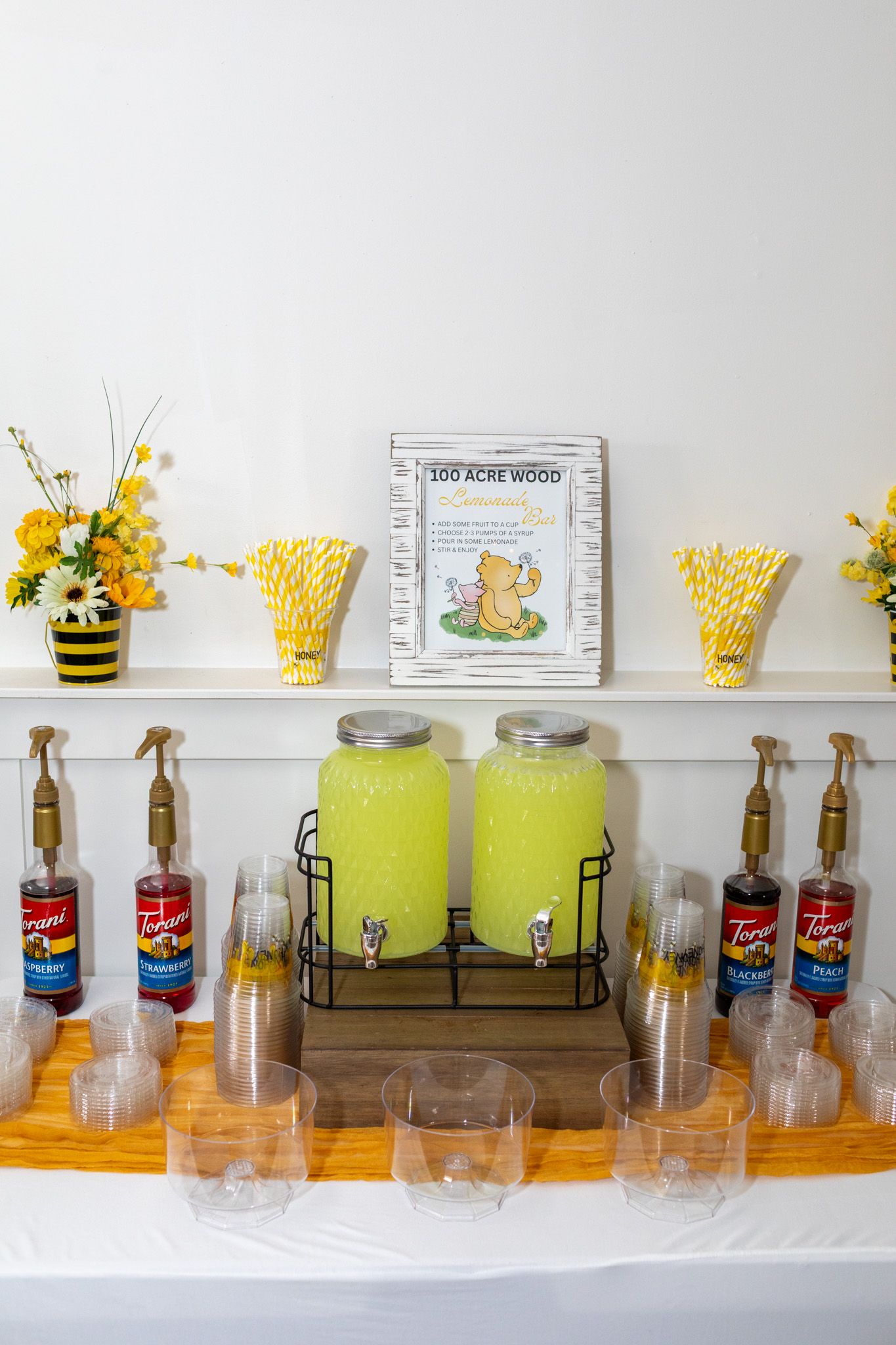 Baby shower drink station with lemonade dispensers, Torani syrups, and yellow floral arrangements.