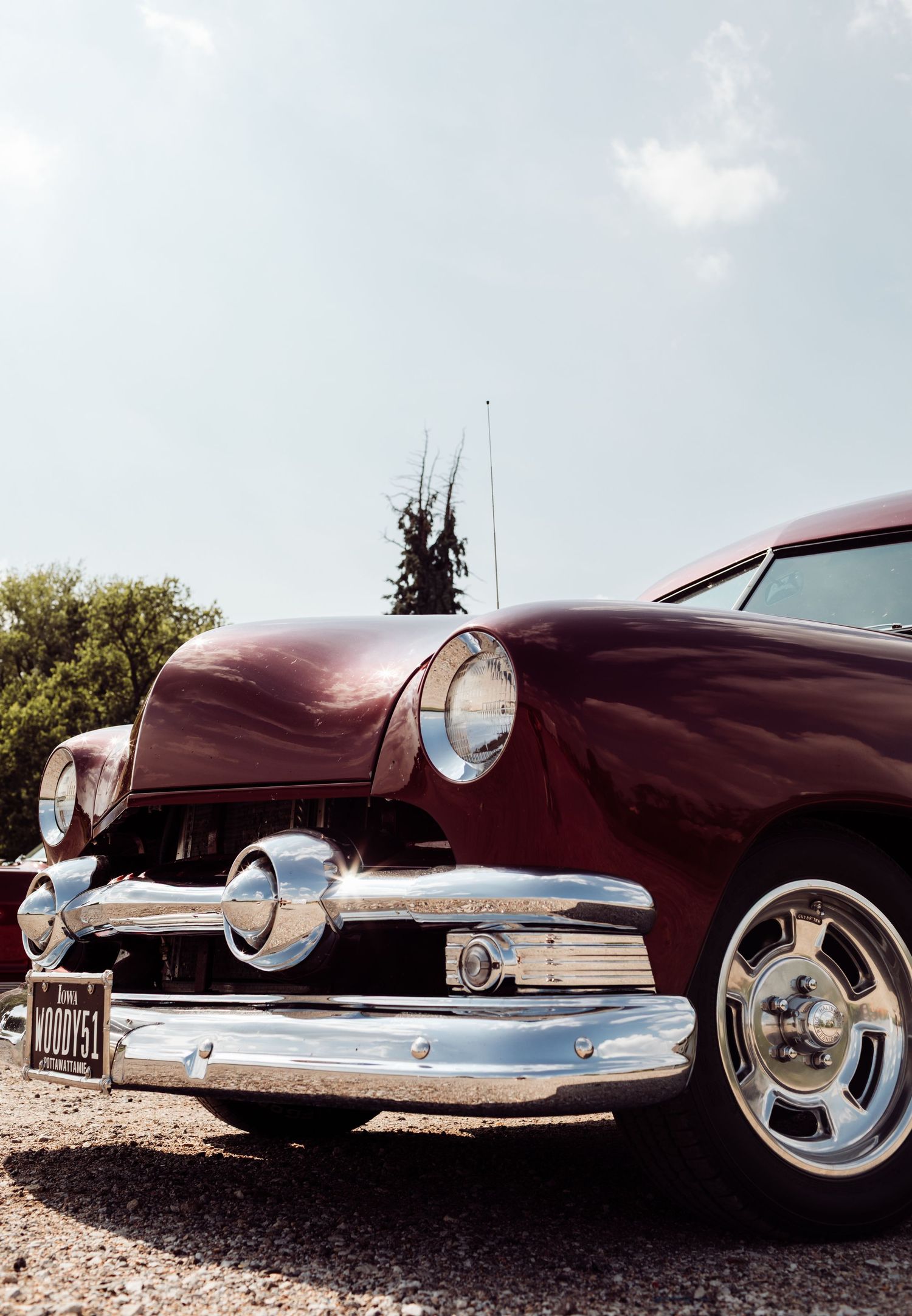 A gleaming burgundy vintage Ford classic car with chrome bumper and headlights photographed from low angle against blue sky.