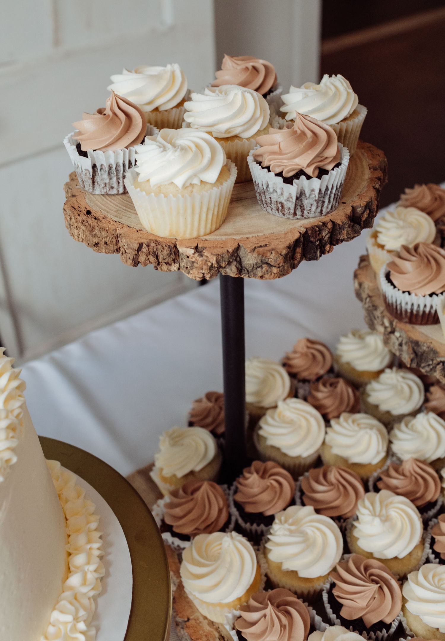 Elegant wedding cupcake tower display with white and chocolate frosted cupcakes on rustic wooden slice stands.