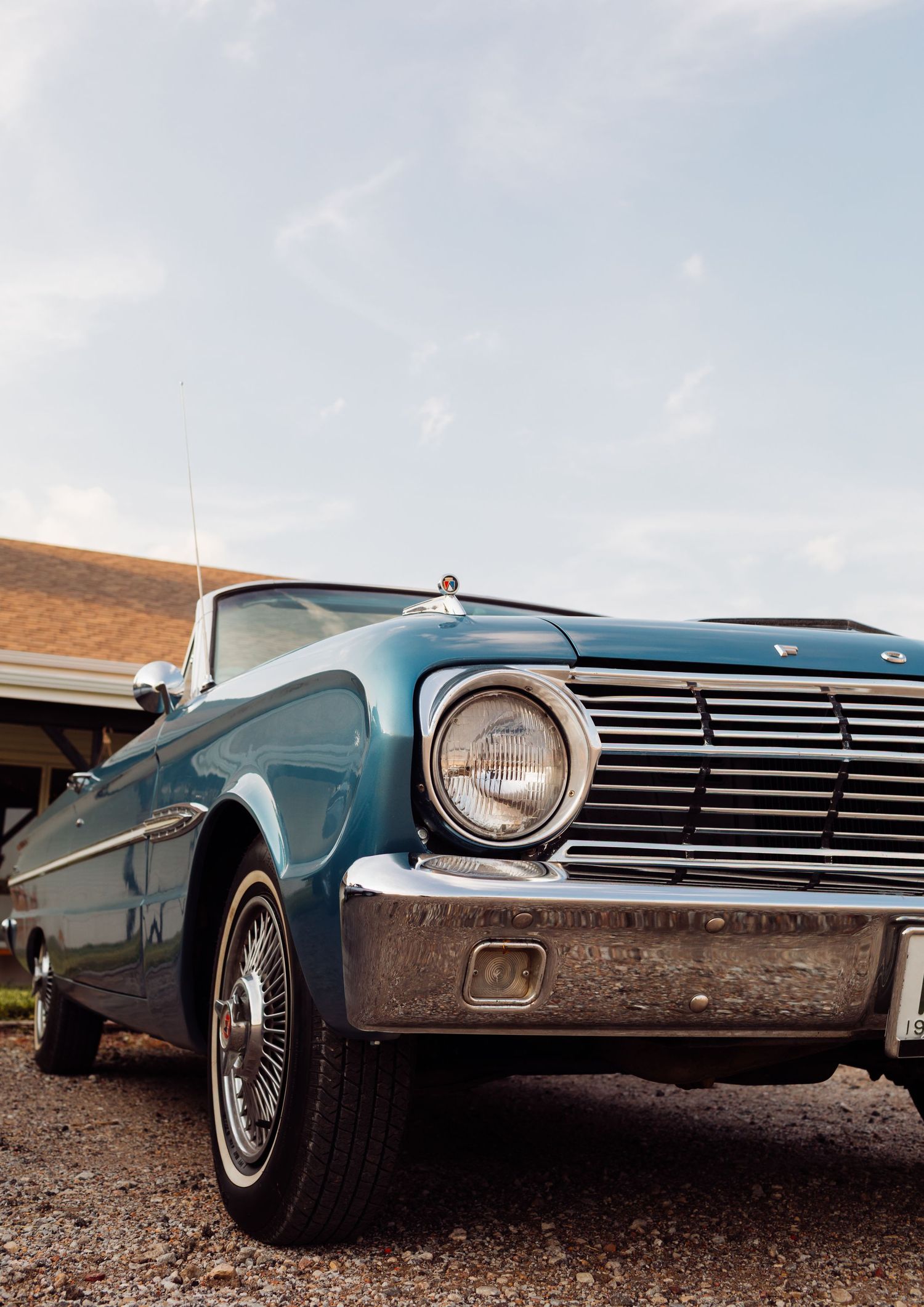A classic teal blue Ford Falcon convertible photographed from low angle against a light blue sky near a building.
