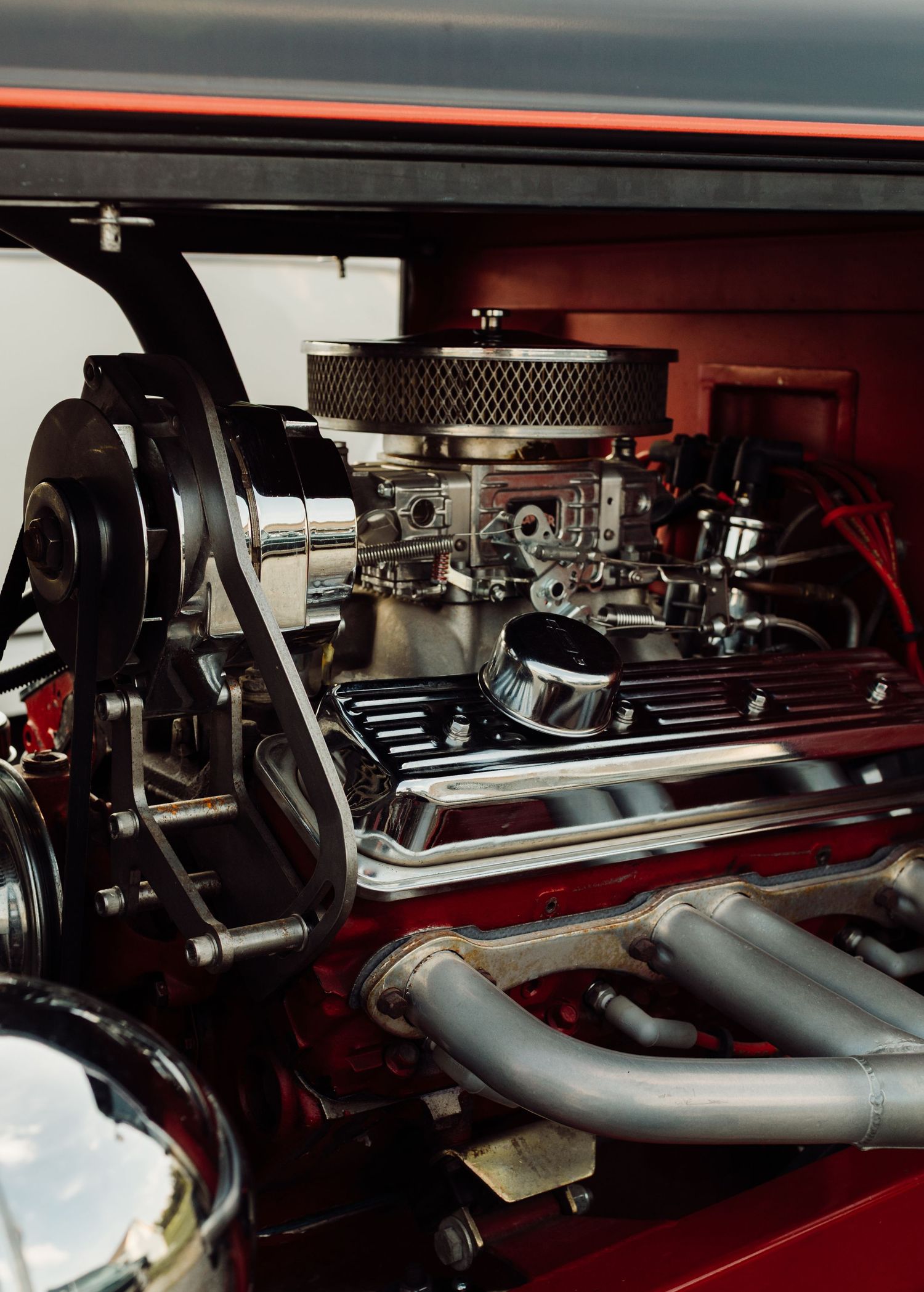 Close-up of a polished high-performance V8 engine with chrome carburetor and headers in a classic red hot rod.