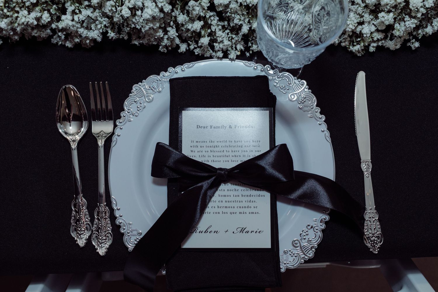 Black and white wedding place setting with ornate silverware and ribbon-tied menu card.