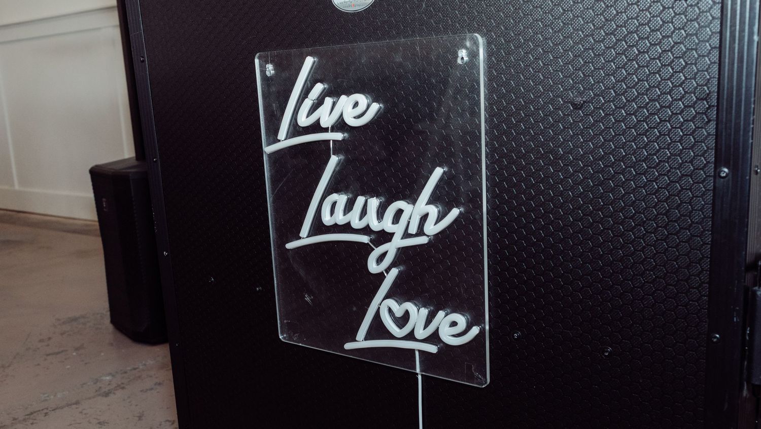 Acrylic Live Laugh Love sign displayed on a black DJ booth at a wedding.