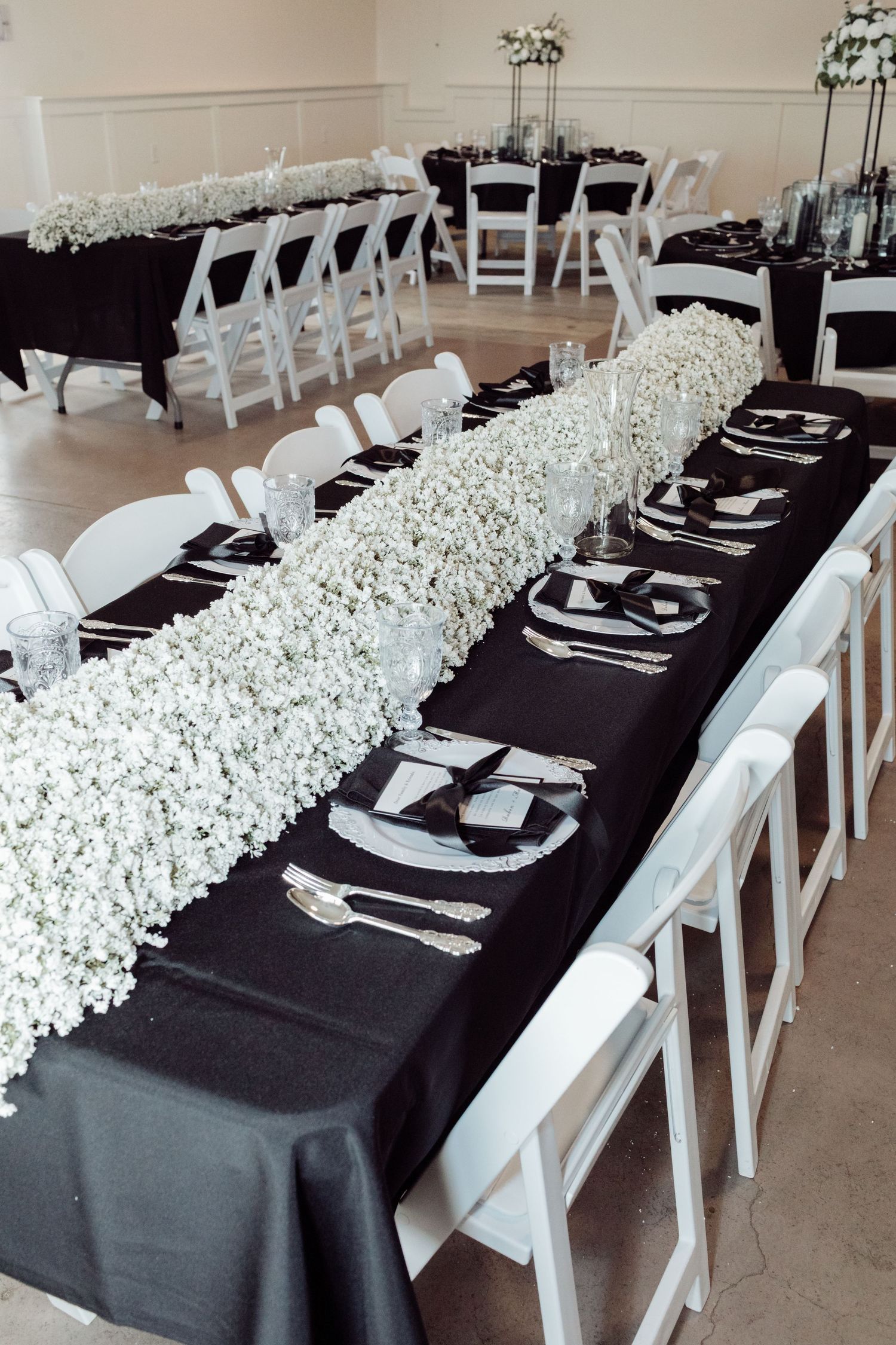 Long black tablecloth banquet tables with white baby's breath runners and white folding chairs.