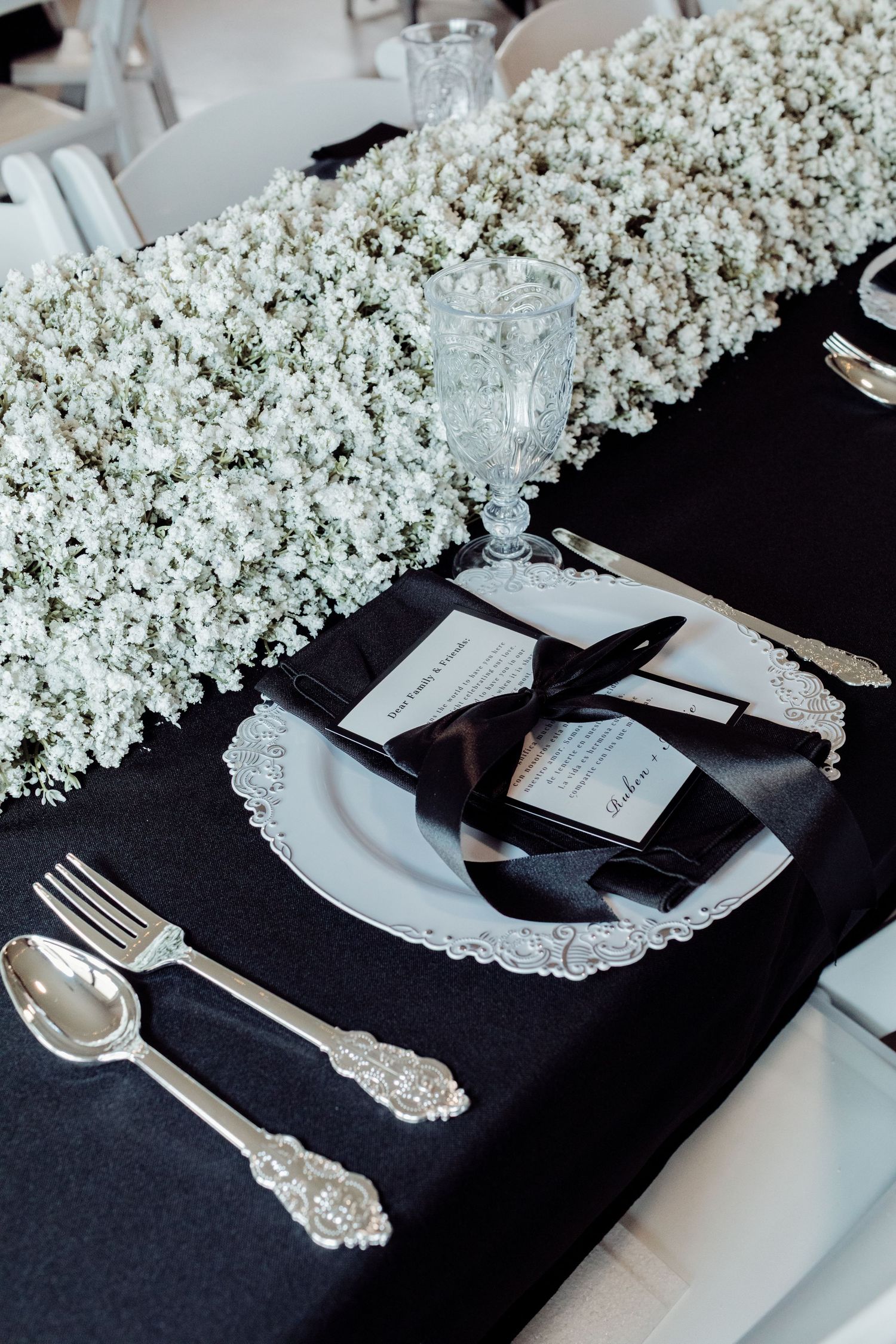 Elegant wedding place setting with crystal glassware, black ribbon napkin, and baby's breath centerpiece.