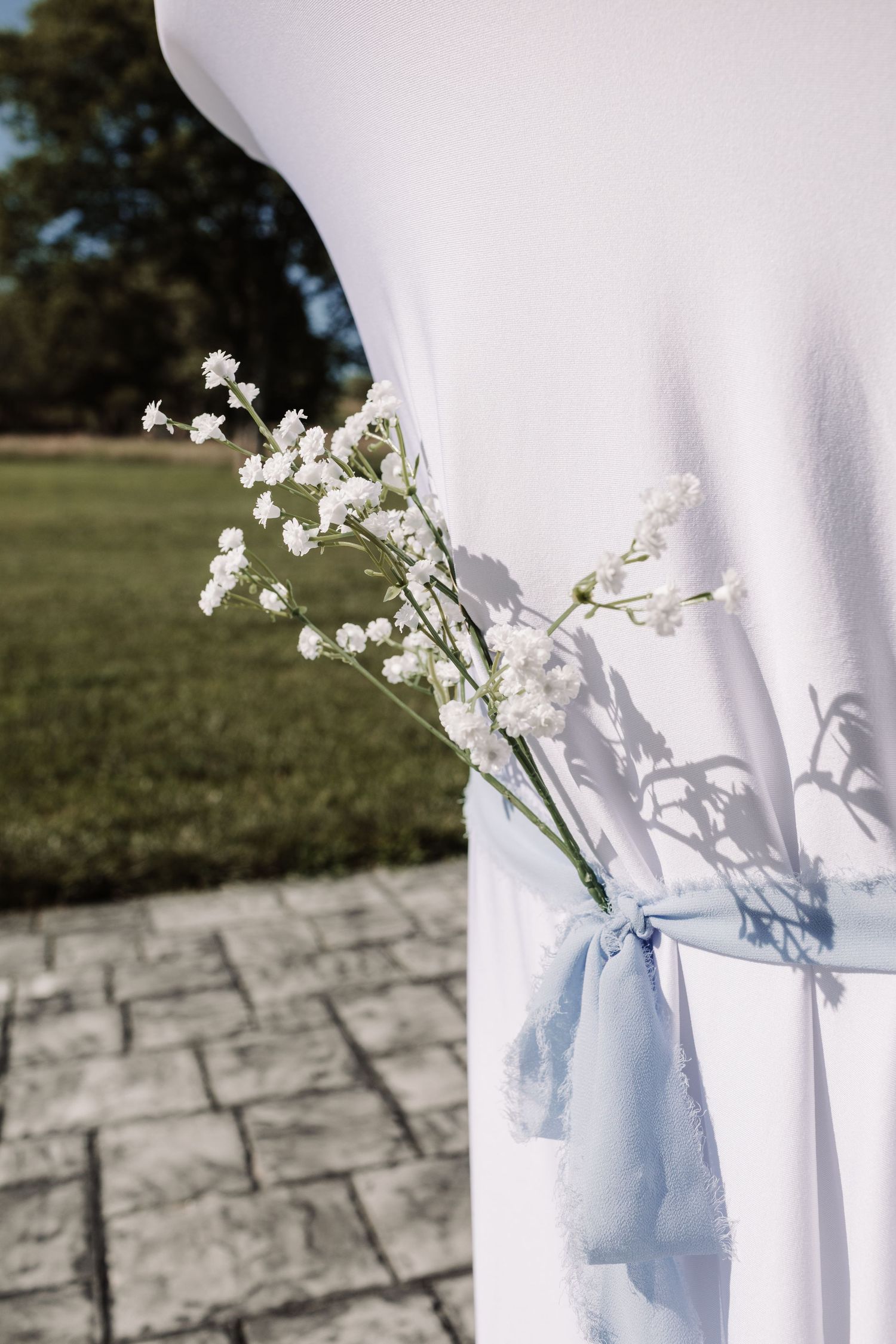 White wedding arch drape tied with a light blue ribbon and baby's breath flowers on a stone patio.