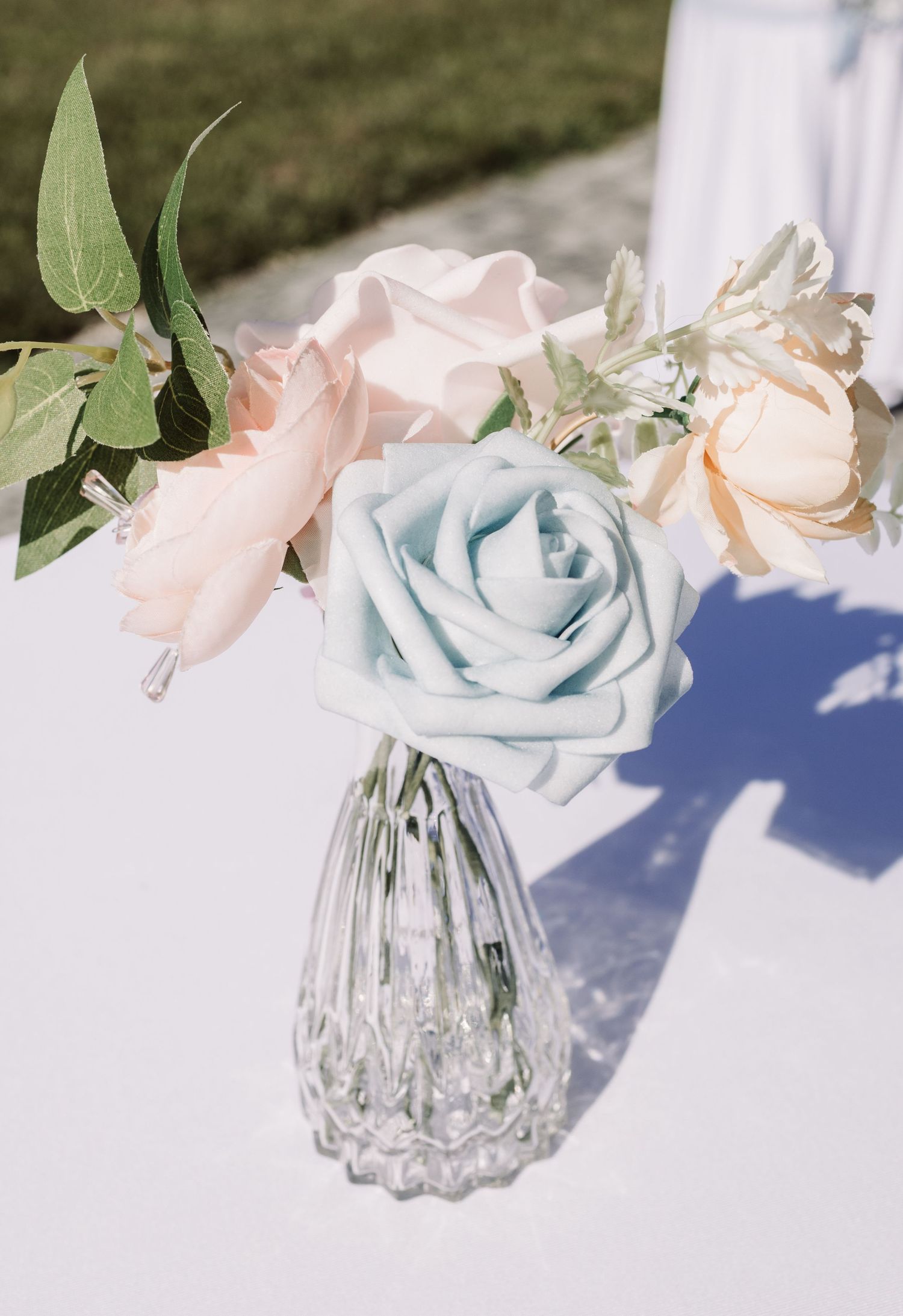 Delicate wedding floral arrangement featuring a light blue rose and blush pink flowers in a crystal vase.
