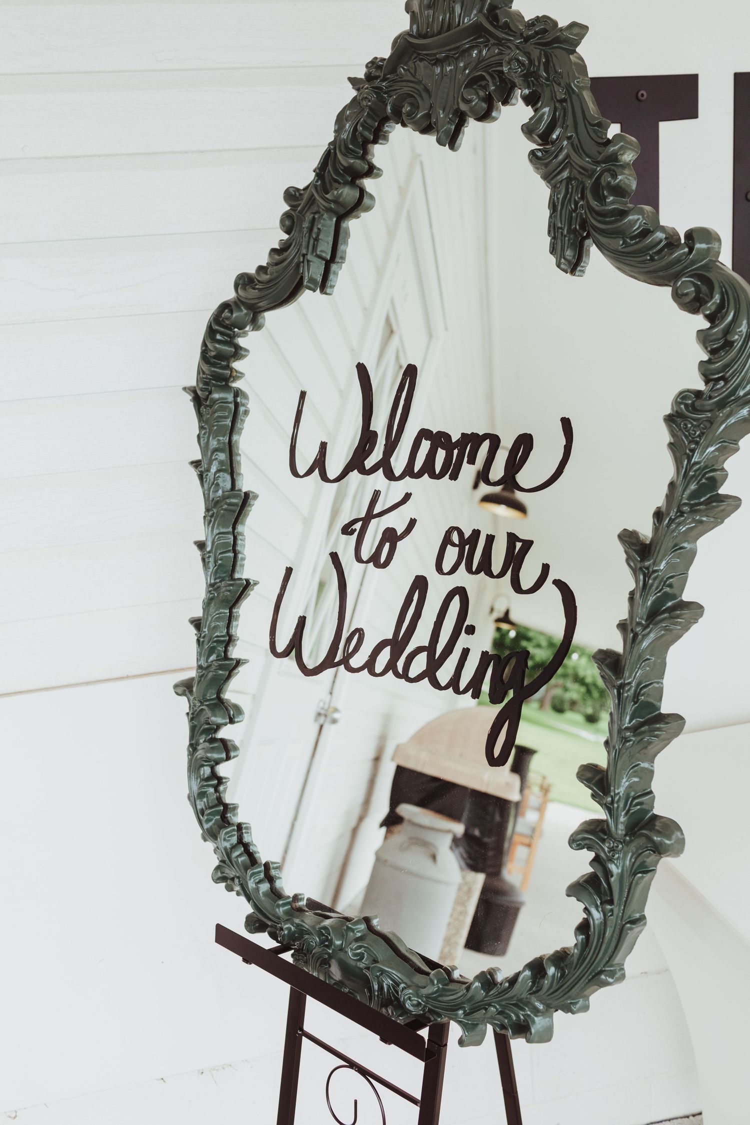 Ornate vintage green mirror on easel displaying Welcome to our Wedding calligraphy sign.