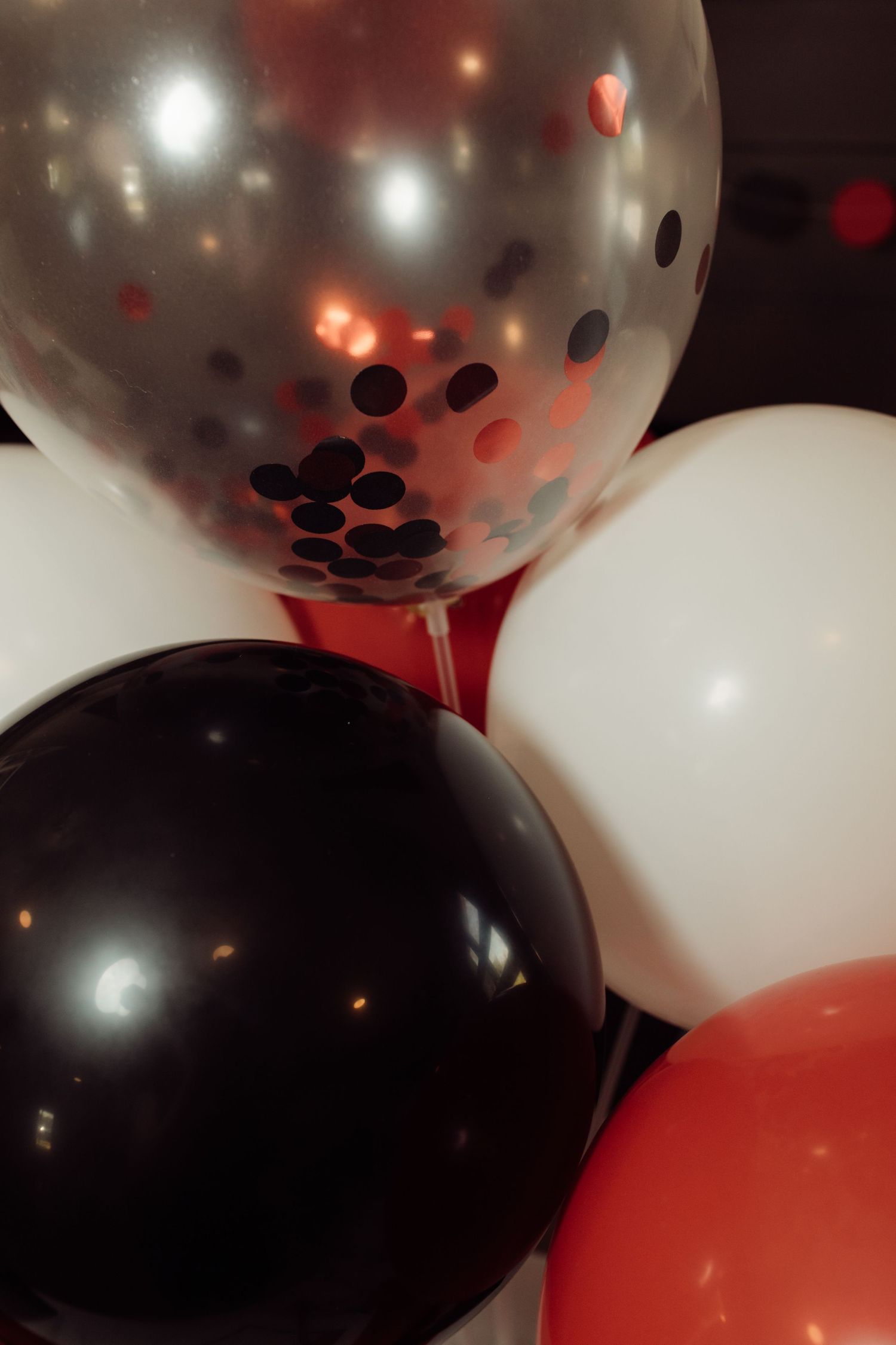 Cluster of black, white, red, and confetti-filled balloons against a dark background for a celebration.