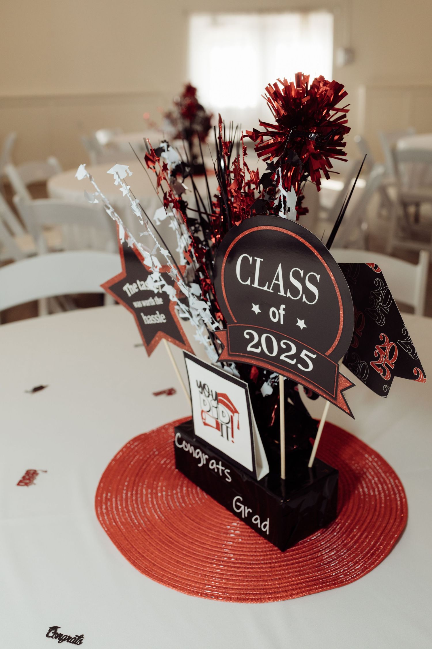 Class of 2025 graduation party centerpiece with red and black decorations, star picks, and confetti on a red charger.