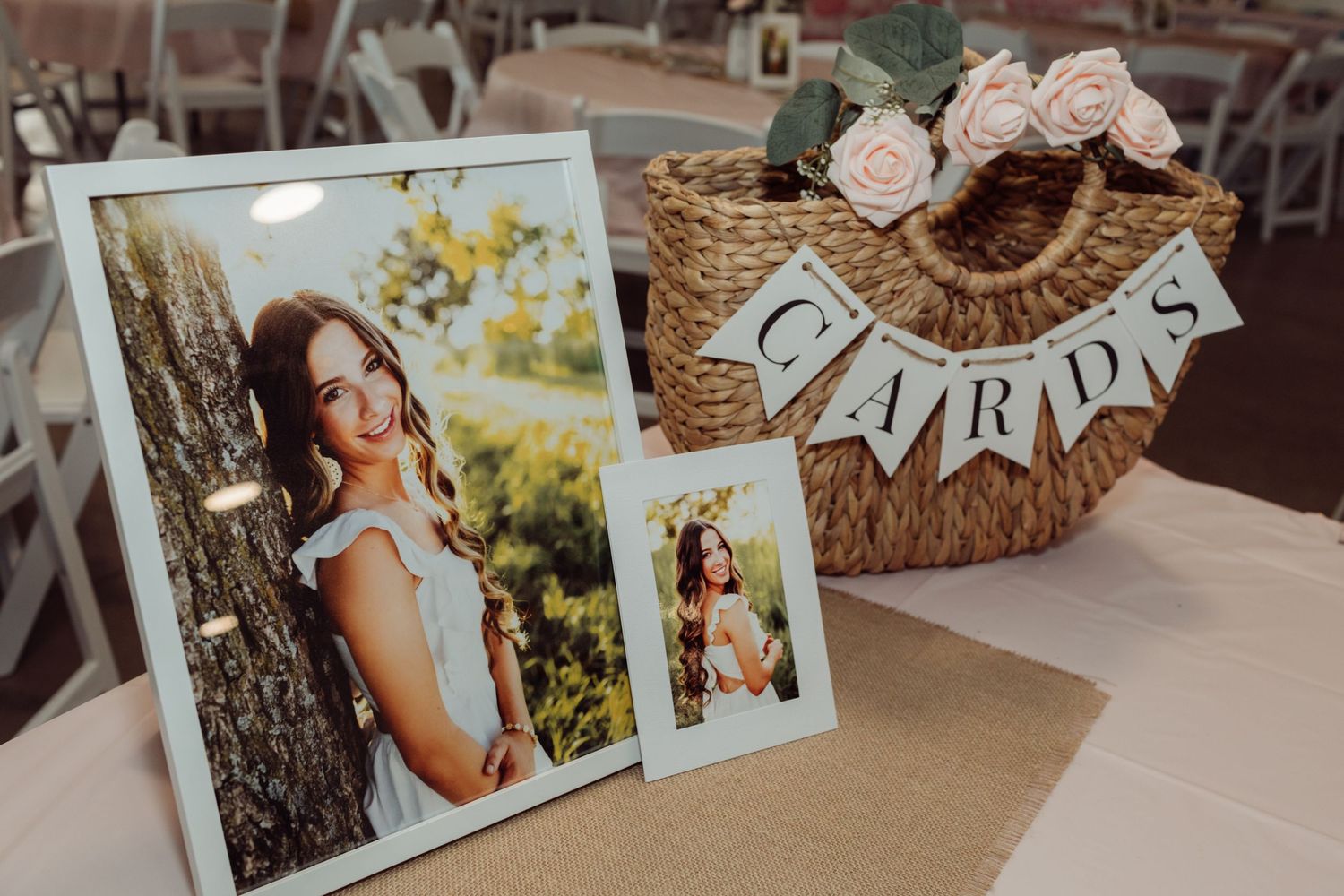 Graduation party card basket with burlap banner and pink roses beside framed senior photos on a table.