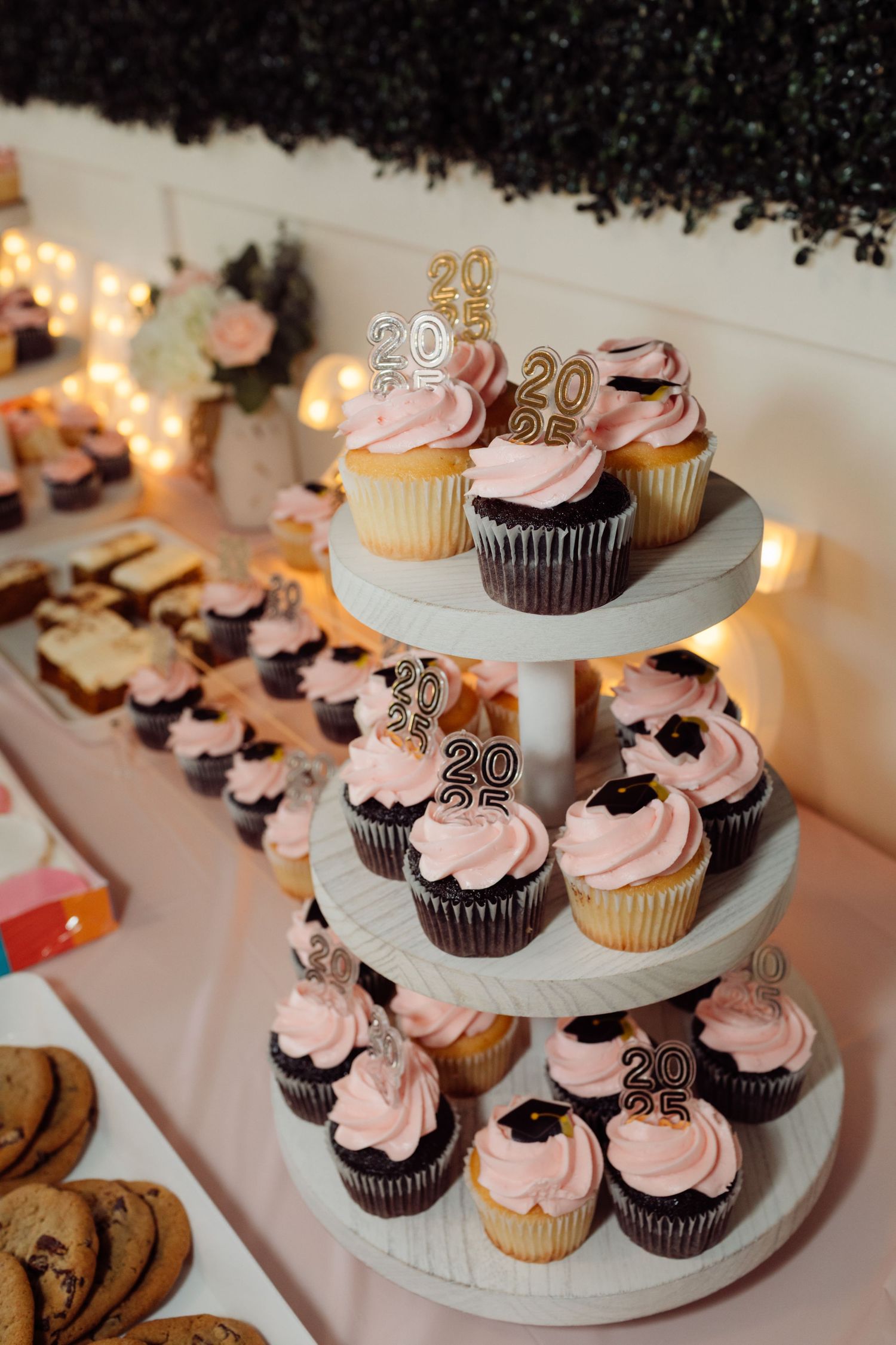 Three-tier white cupcake stand with pink frosted cupcakes topped with gold 2025 graduation cap toppers.