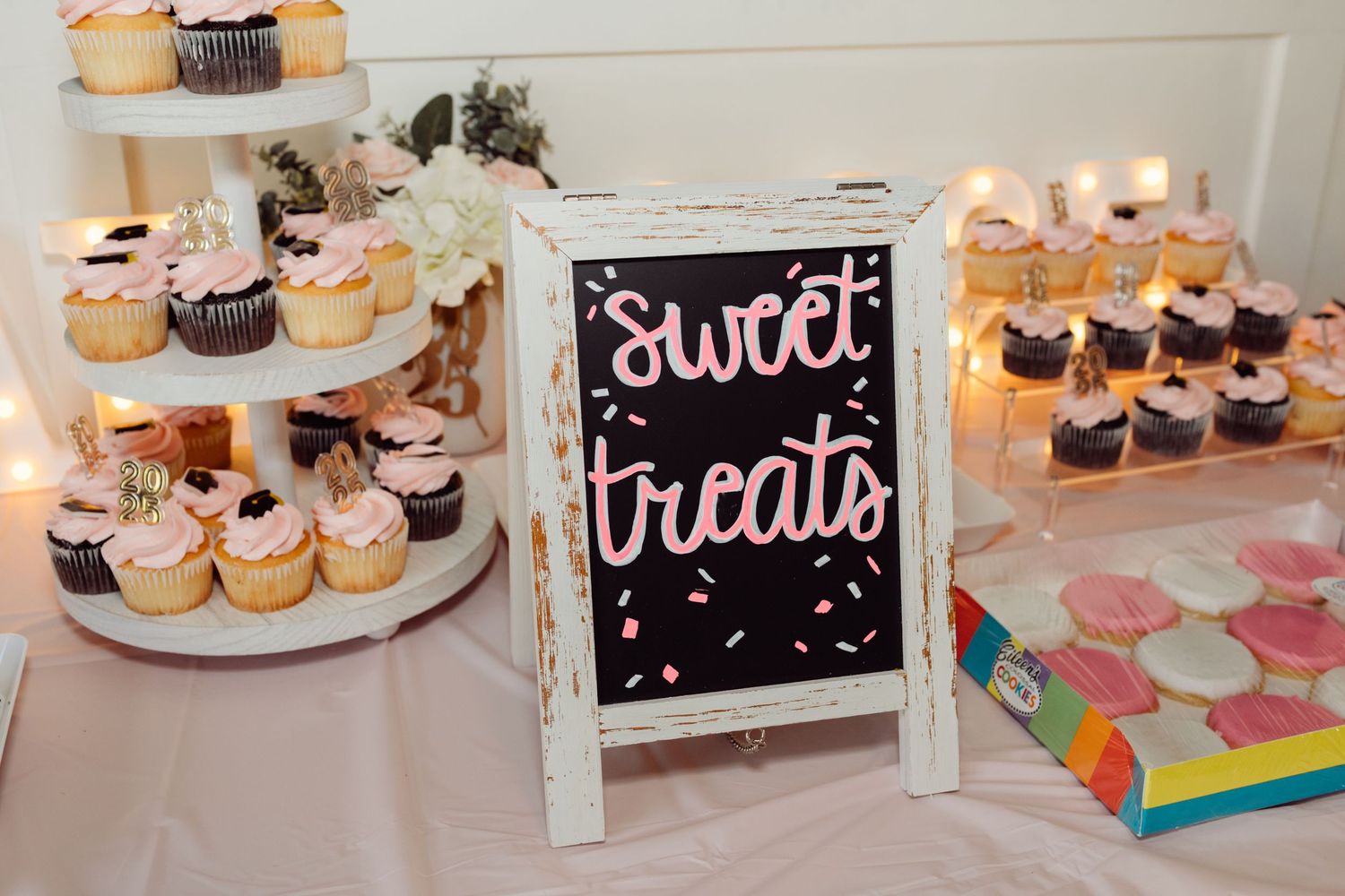 Sweet treats dessert table with cupcakes and a chalkboard sign at a pink and white graduation party.