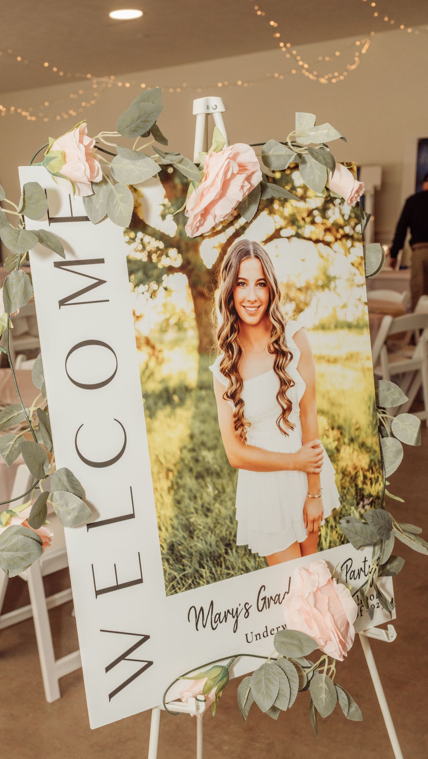 Welcome sign with senior portrait framed in pink roses and eucalyptus for Mary's graduation party.